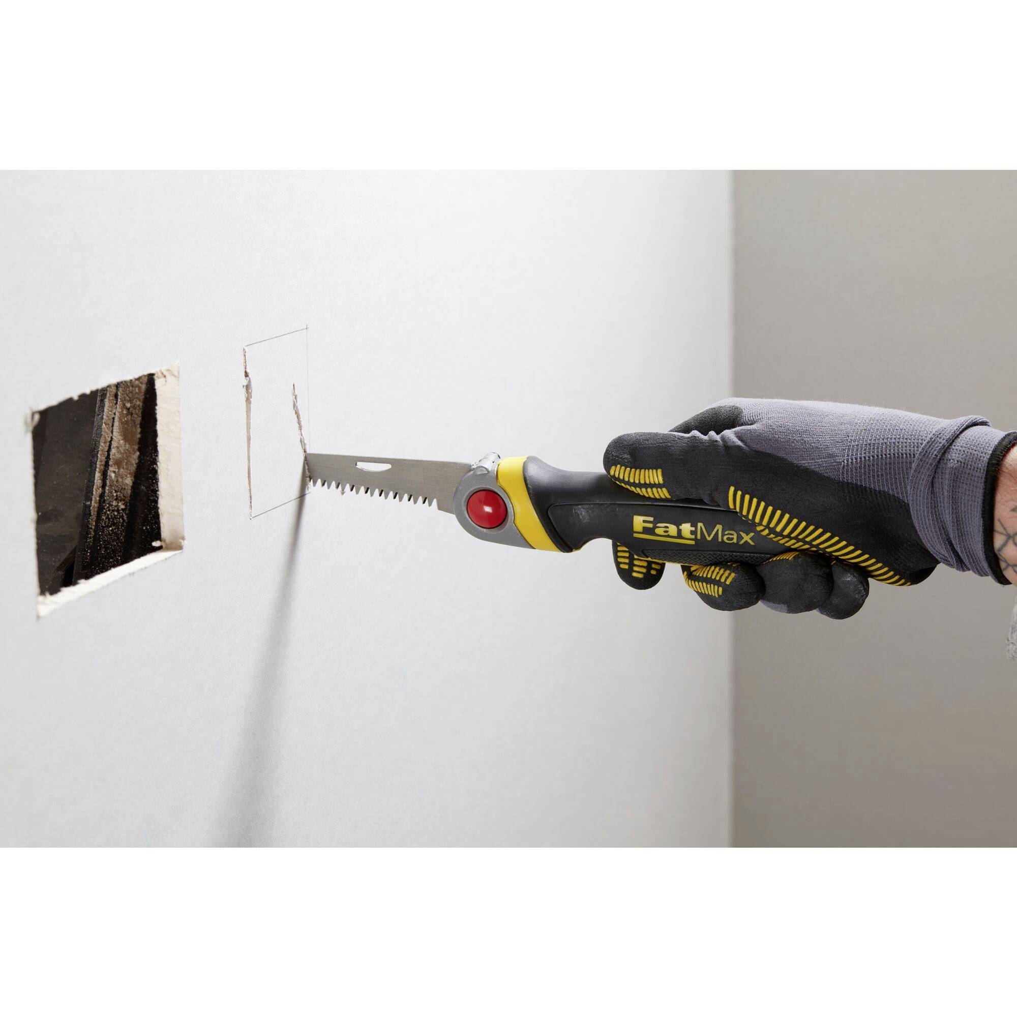 Une personne portant des gants découpe un trou rectangulaire dans une cloison de plaque de plâtre à l'aide d'une scie.