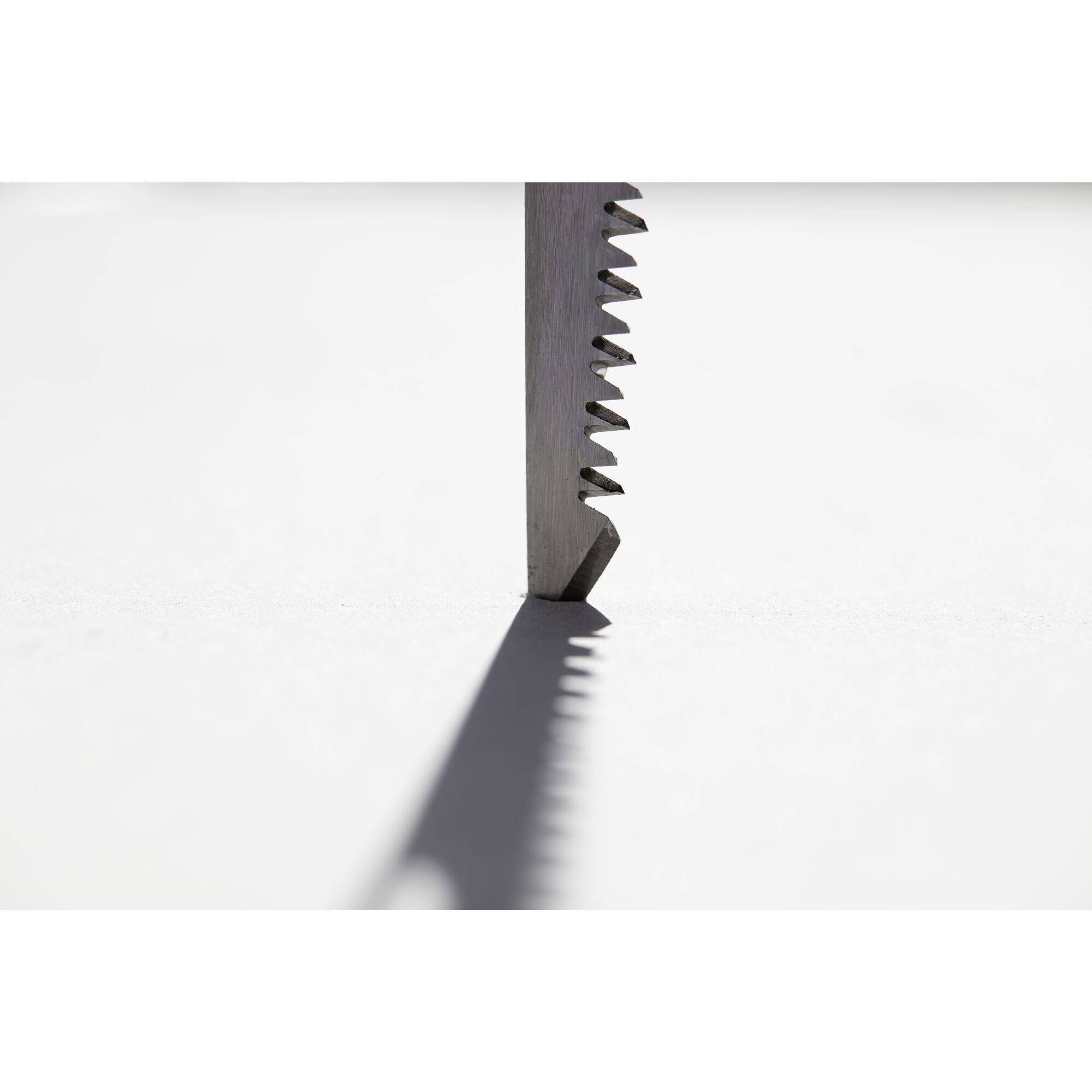 Gros plan sur la pointe d'une lame de scie, positionnée verticalement, avec des dents projetant une ombre sur une surface blanche lisse.