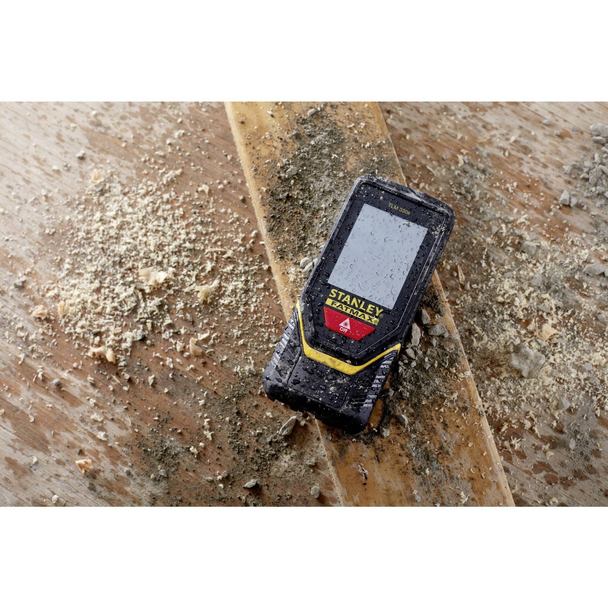 Un télémètre laser repose sur un support en bois poussiéreux, entouré de sciure, suggérant un environnement de chantier.