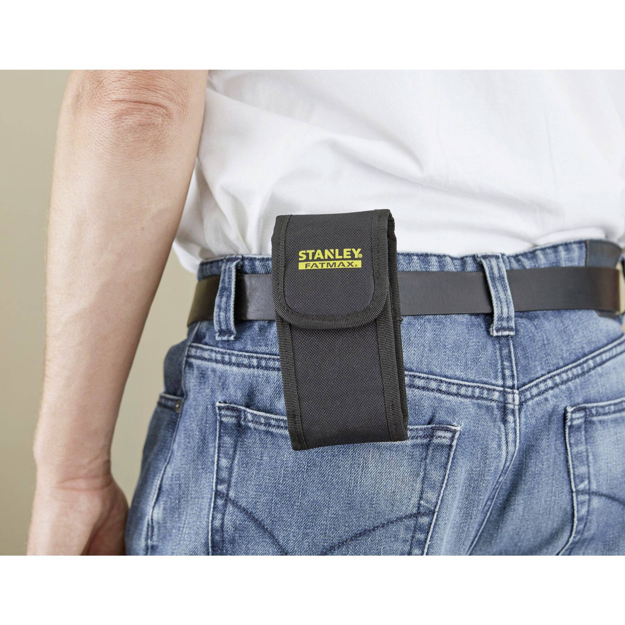 Une personne porte un sac Stanley Fatmax noir à sa ceinture en cuir, accroché sur son jean au niveau de la hanche droite.