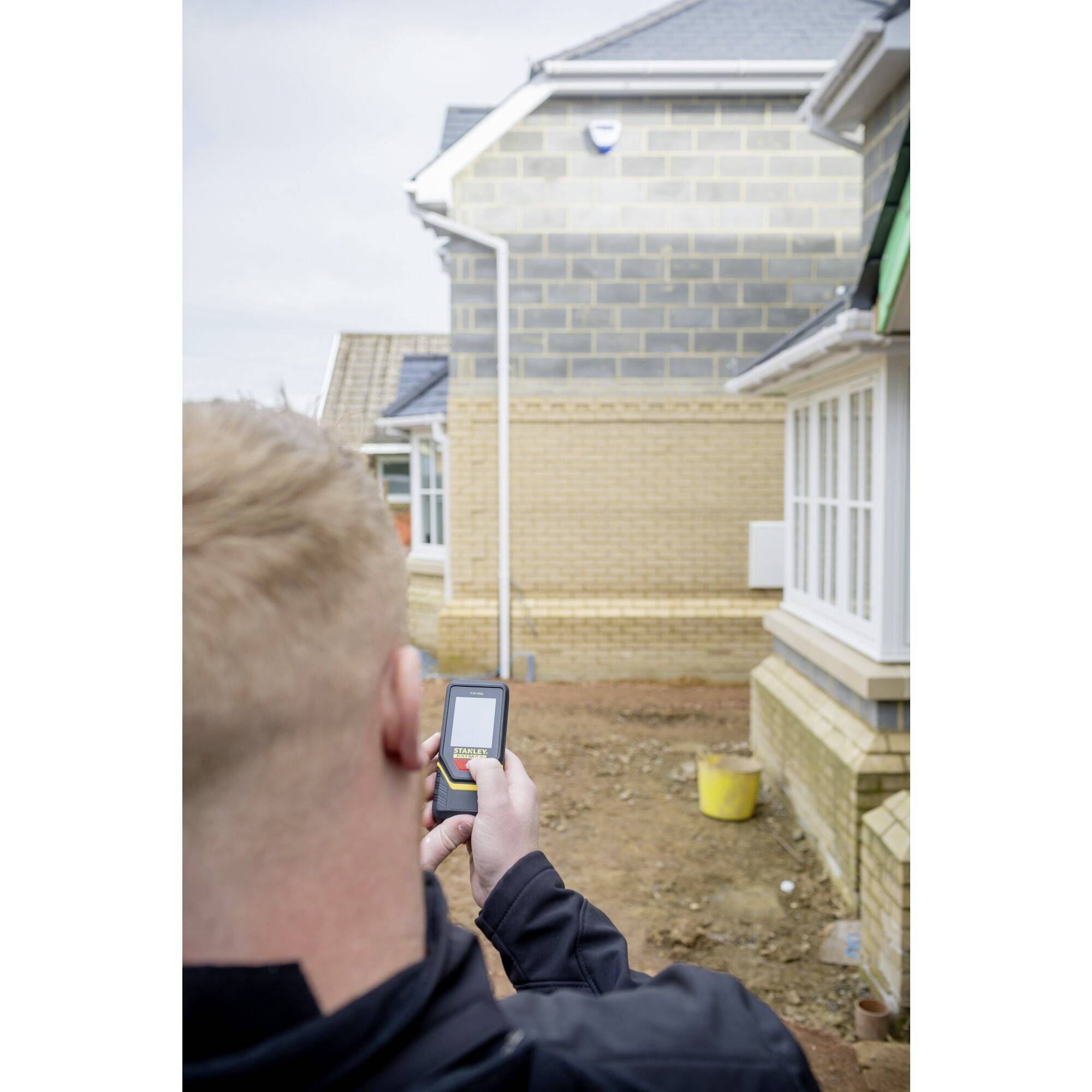 Une personne tient un télémètre laser et mesure la distance jusqu'à une maison en briques partiellement construite sur un chantier de construction.