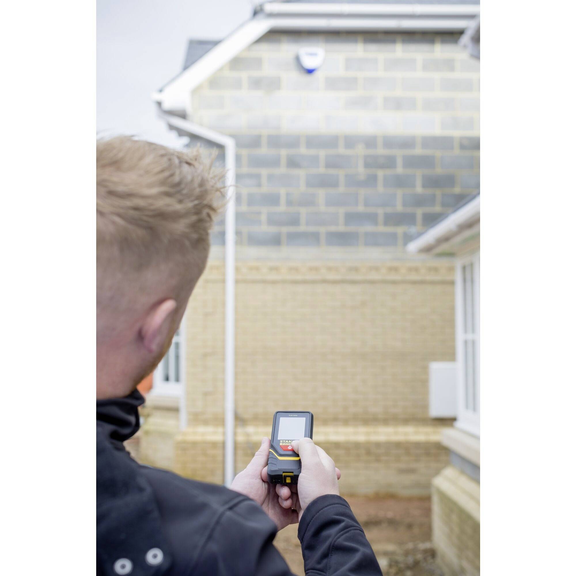 Une personne mesure la distance jusqu'à un mur d'une maison nouvellement construite à l'aide d'un appareil laser. Le mur est composé de briques.