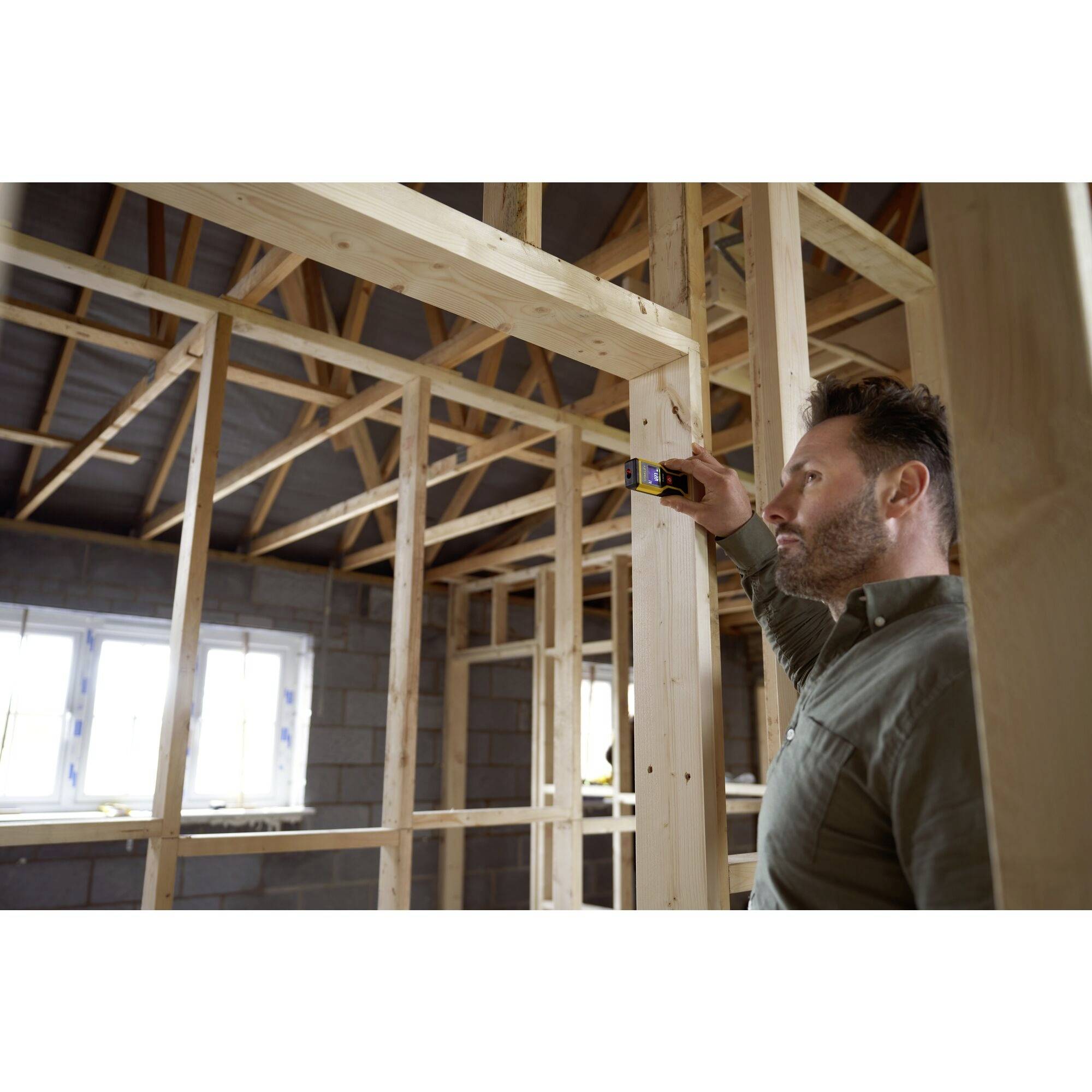 Un homme mesure la distance à l'aide d'un télémètre laser dans un bâtiment à ossature bois en construction.