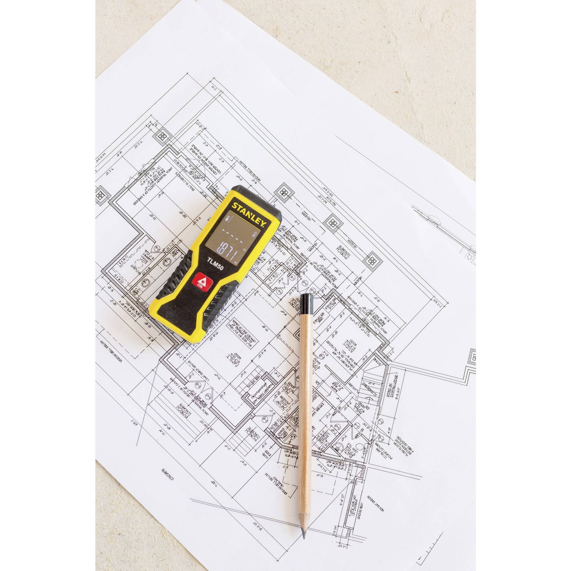 Un télémètre laser et un crayon sont posés sur un plan architectural. Le plan présente des plans détaillés d'un bâtiment.