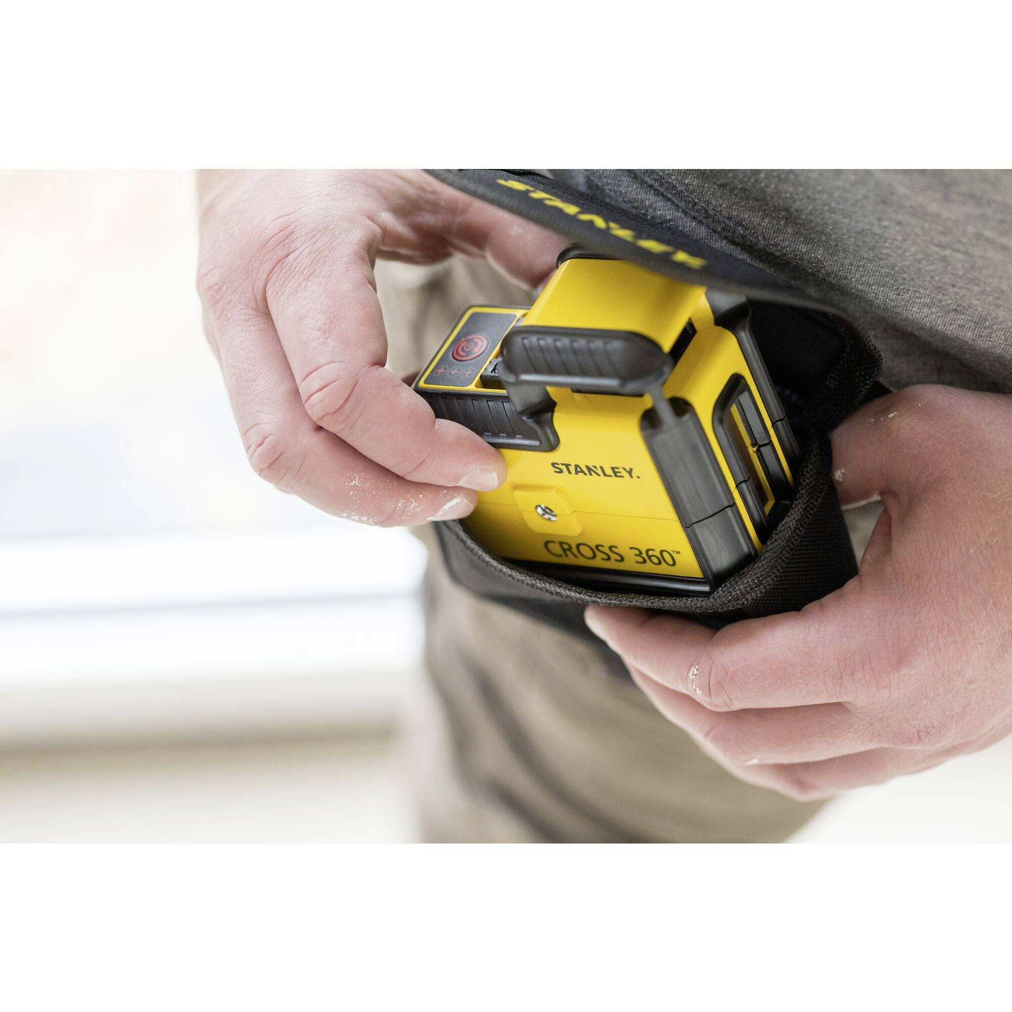 Une personne tient un appareil de mesure laser jaune dans ses mains, prêt à être utilisé. L'appareil est de la marque Stanley.