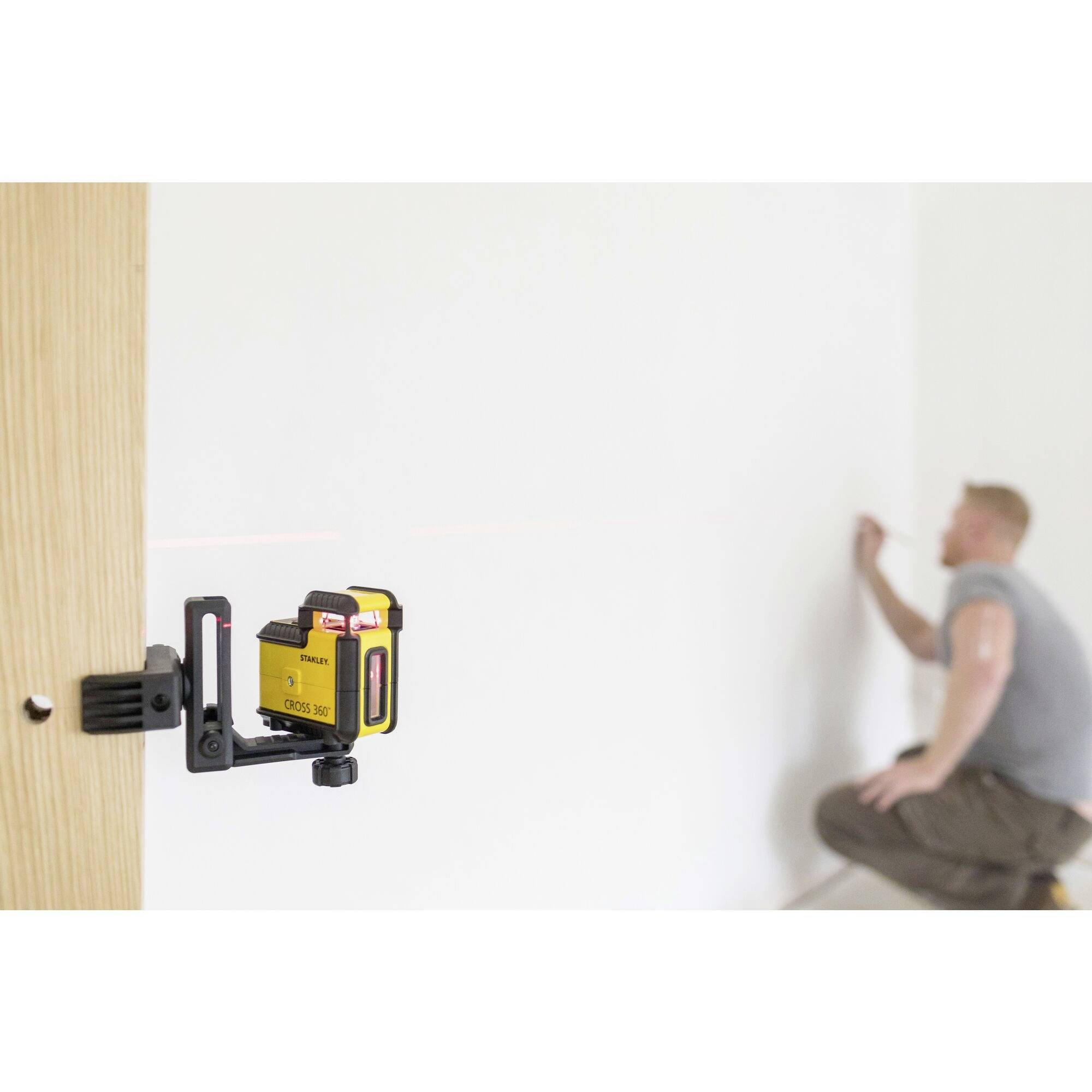 Une personne aligne une ligne droite sur un mur blanc à l'aide d'un appareil de nivellement laser jaune.