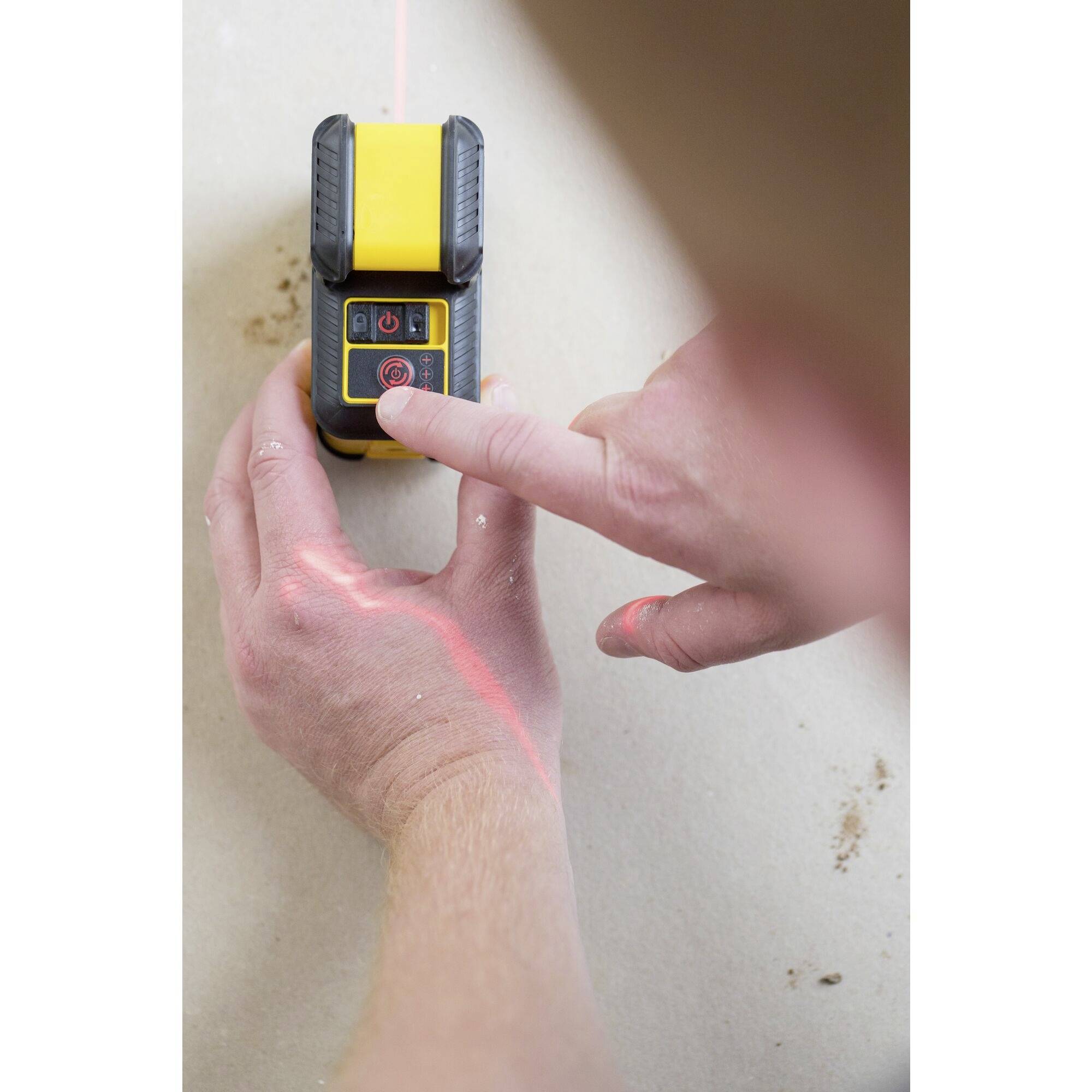 Une personne utilise un appareil de mesure laser jaune pour aligner une ligne droite sur une surface. Le laser est rouge.