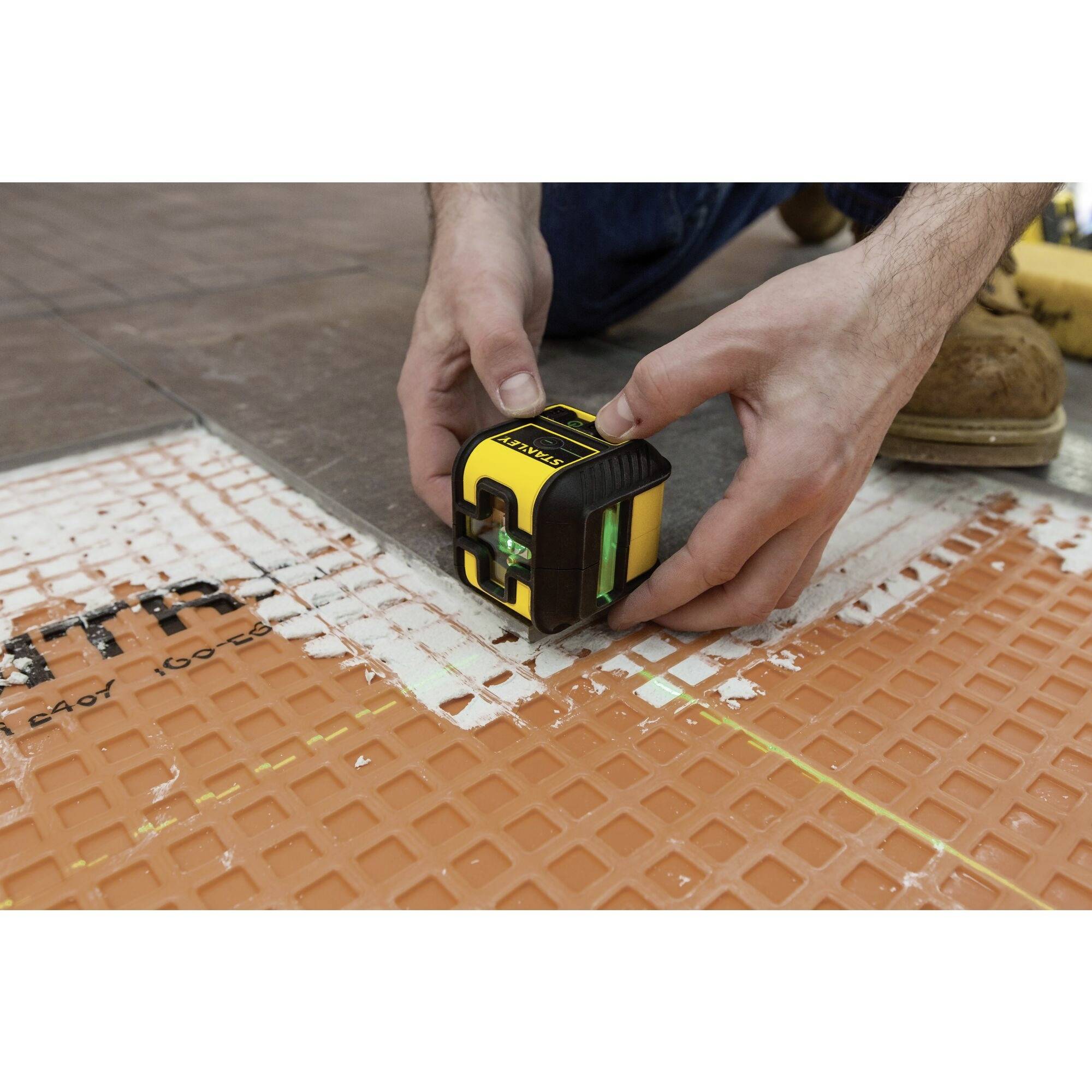 Une personne utilise un outil laser pour mesurer et aligner précisément des carreaux de sol.