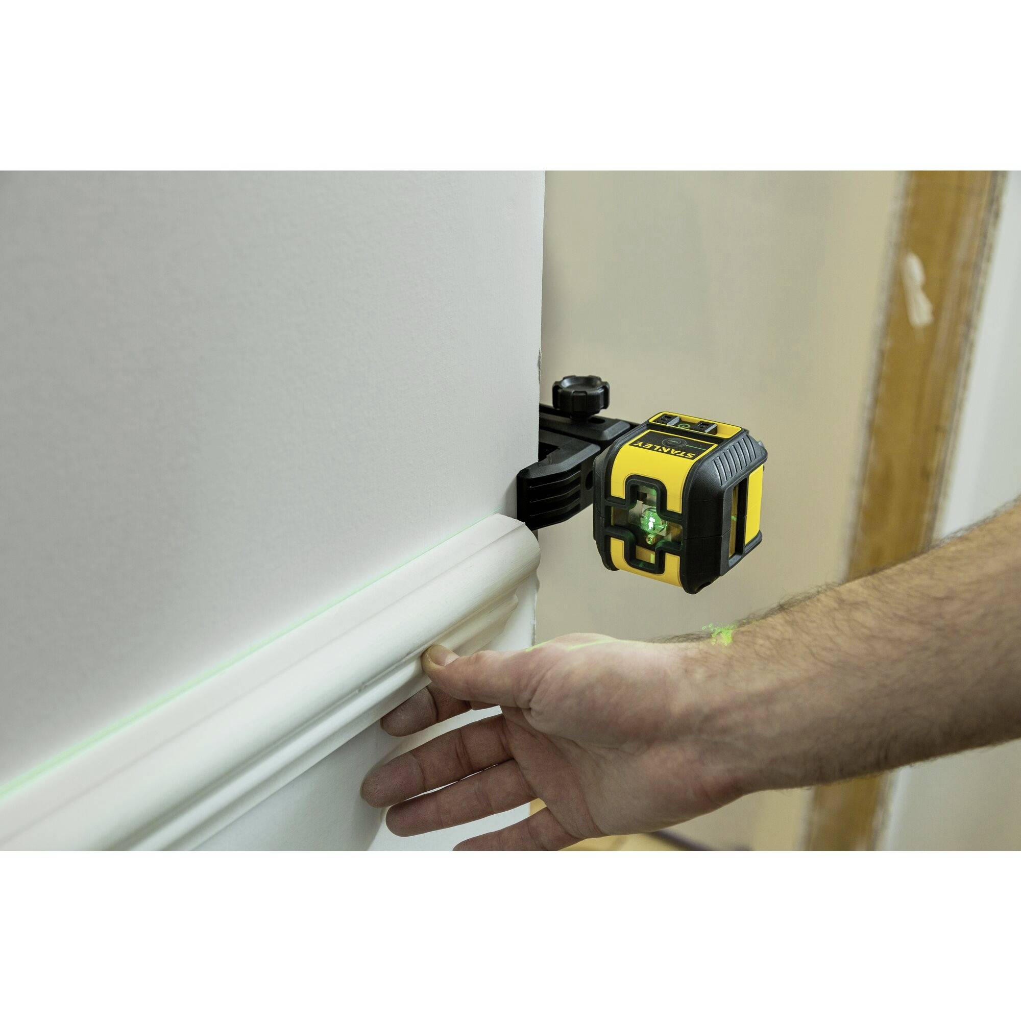 Une personne aligne un niveau à bulle à l'aide d'un outil laser numérique sur un mur. L'appareil projette des lignes vertes.