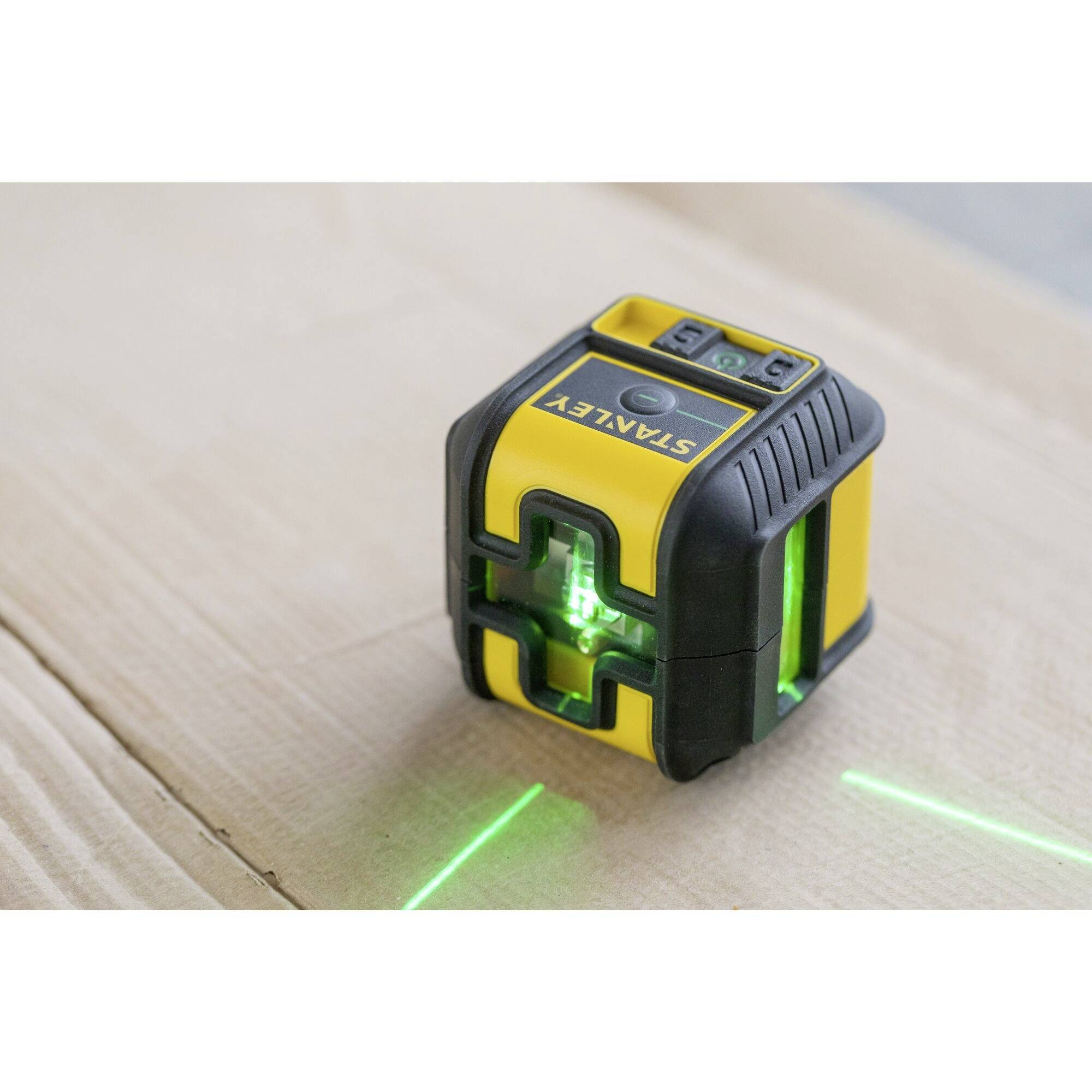 Un appareil de mesure laser jaune et noir projette des lignes vertes sur une surface en bois pour un mesurage précis.