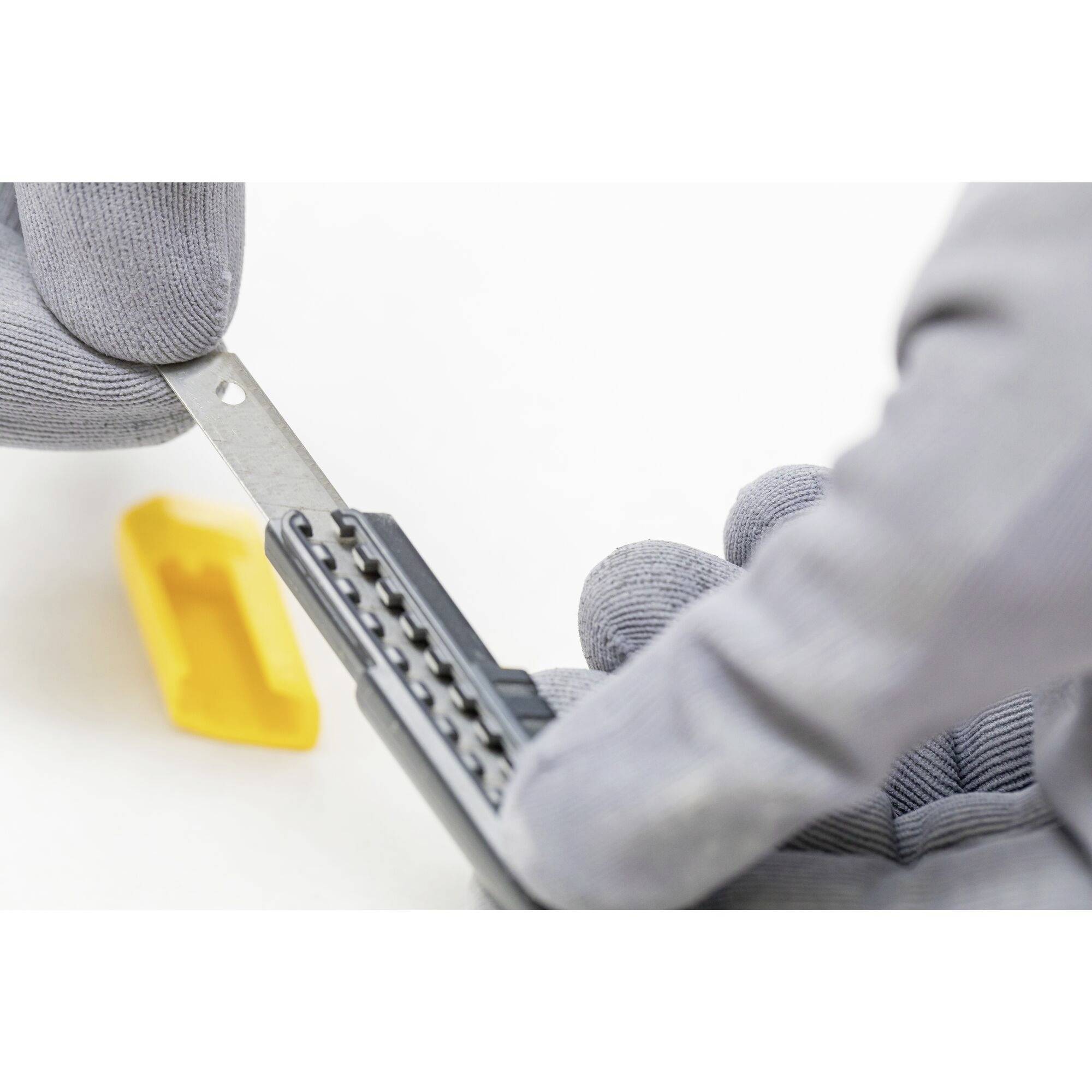 Une main gantée tient un petit outil gris aux bords dentelés, tandis qu'une pièce en plastique jaune est posée à côté.