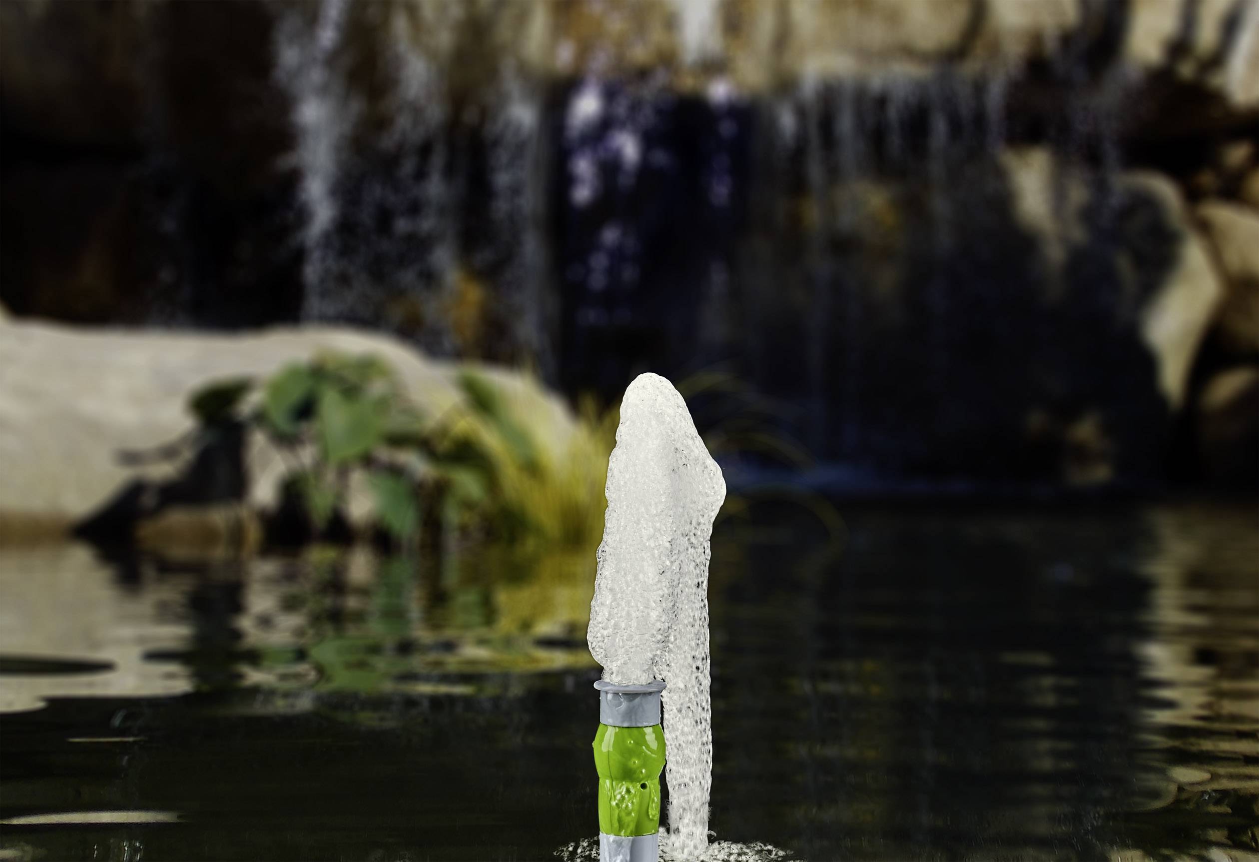 Une fontaine jaillissante dans l'étang, devant une cascade floue en arrière-plan.