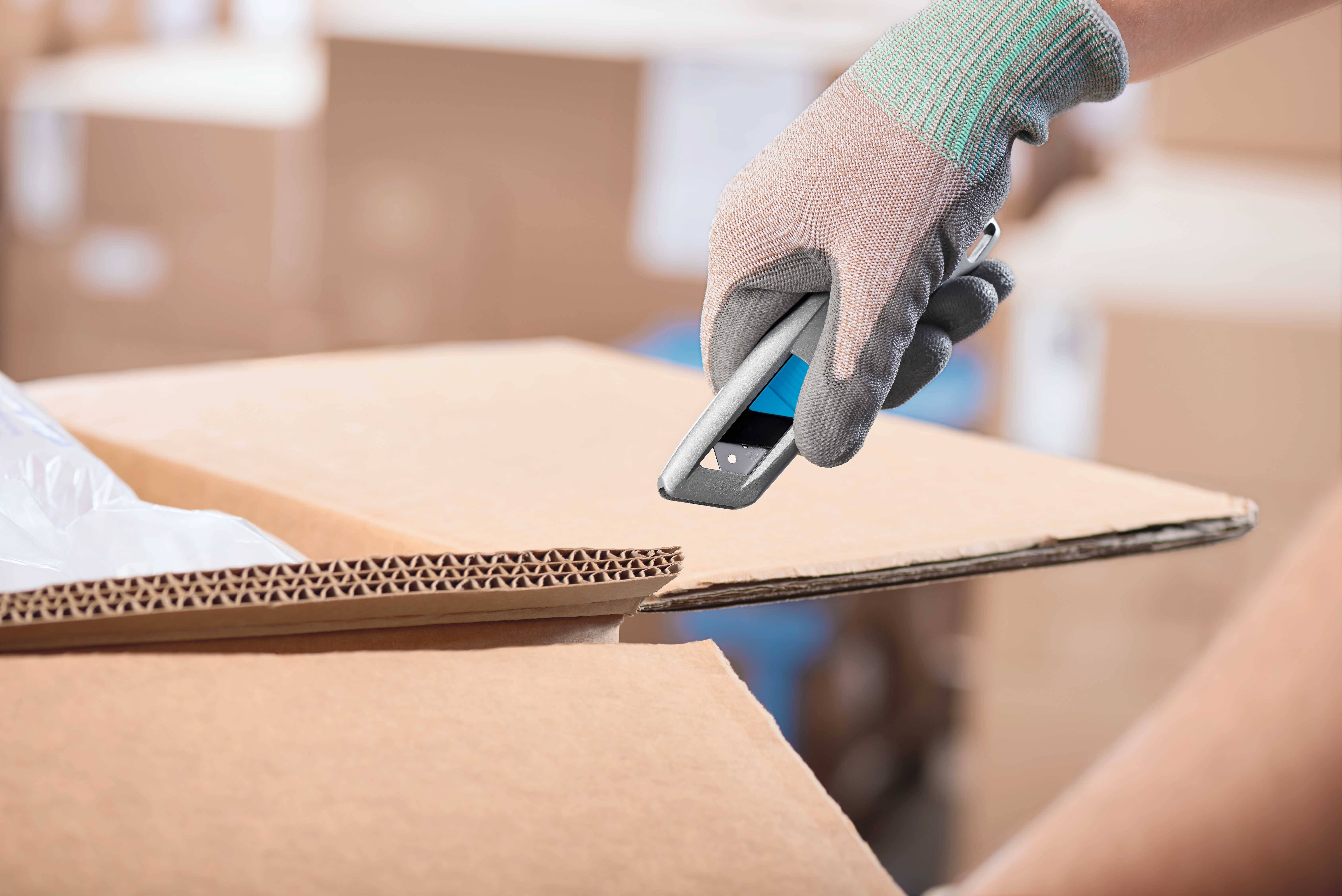 Une main gantée scanne un carton déchiré avec un lecteur de code-barres dans un entrepôt.