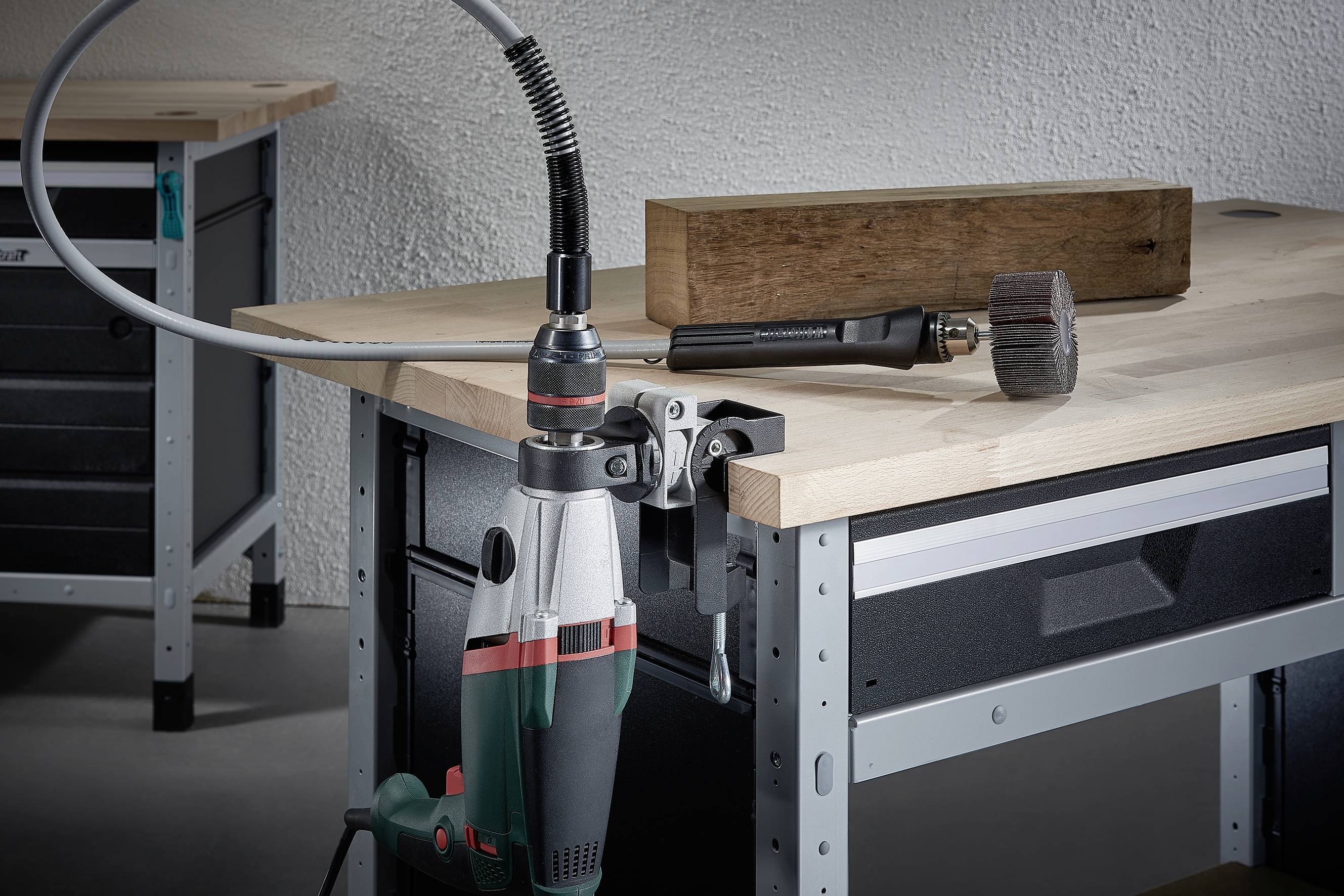Dans un atelier, une perceuse est posée sur une table, à côté d'un bloc de bois et d'un grand outil à vis.