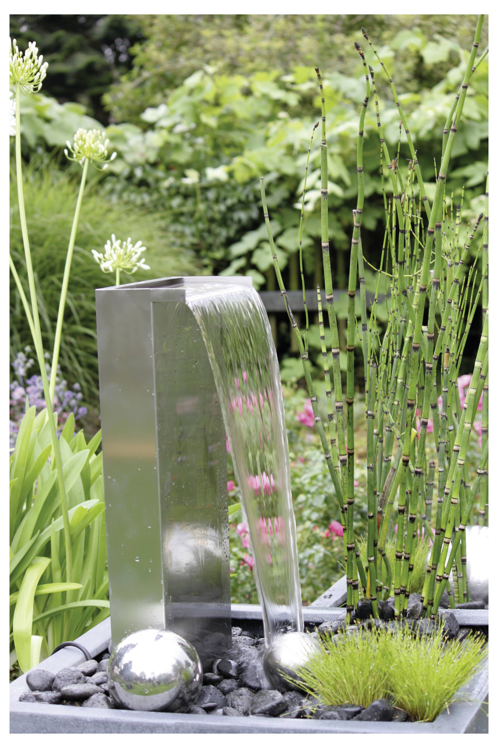 Une fontaine de jardin moderne avec de l'eau s'écoulant d'un bec métallique argenté, entourée de plantes vertes et de fleurs, rehaussant la décoration extérieure.