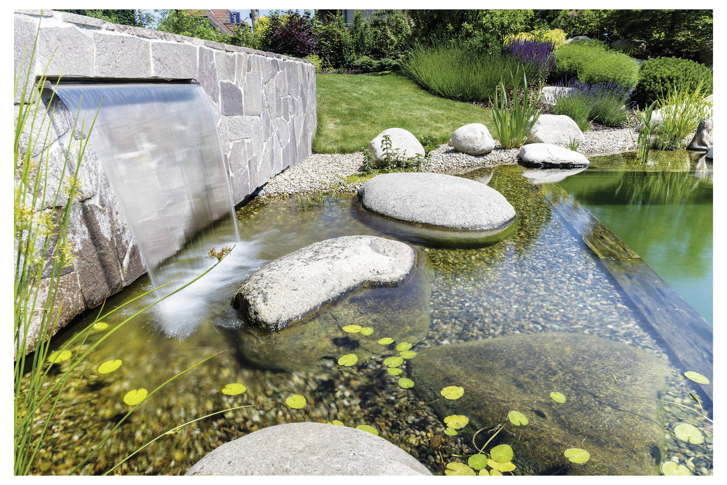 Un étang de jardin paisible avec une cascade, des rochers lisses et une végétation luxuriante. L'eau claire s'écoule sur les rochers, entourée de plantes.
