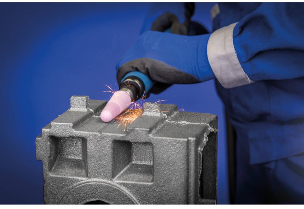 Une personne meule du métal avec une meuleuse d'angle. Des étincelles jaillissent du point de meulage de couleur sable. Gants et vêtements de protection.