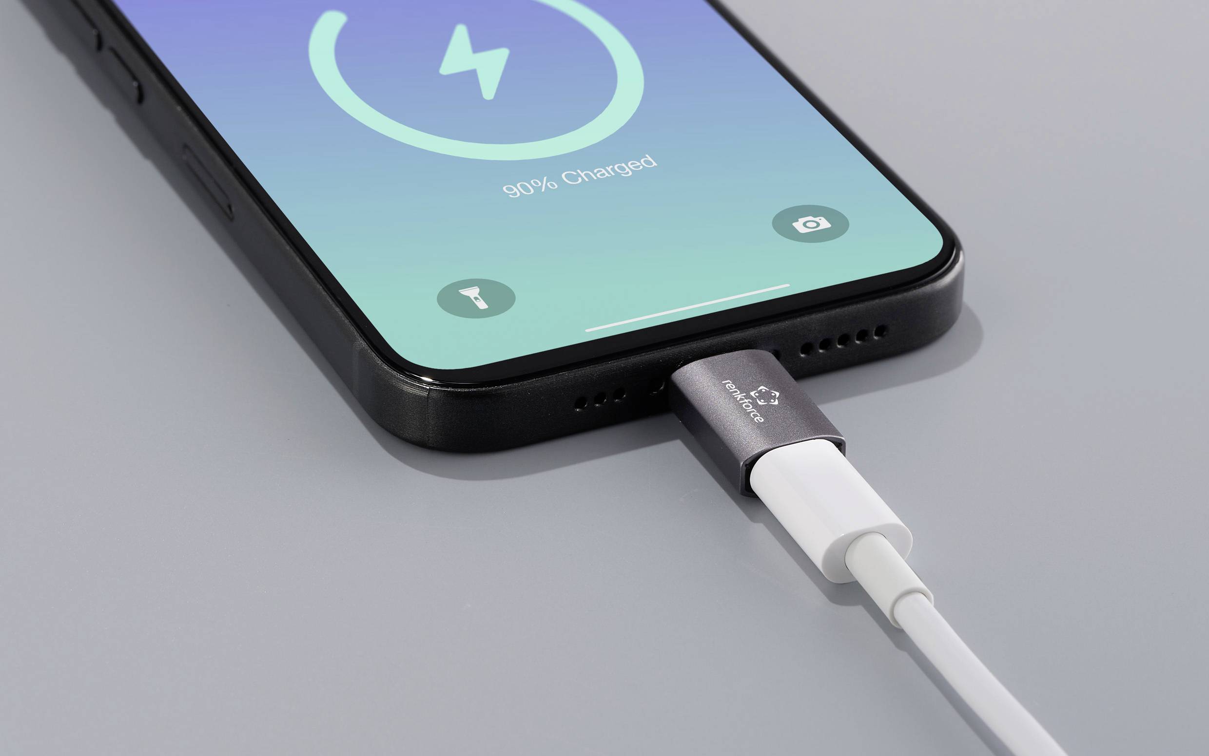 Un smartphone est en train d'être chargé avec un câble. L'écran affiche « 90% chargé », avec un symbole de charge en haut.