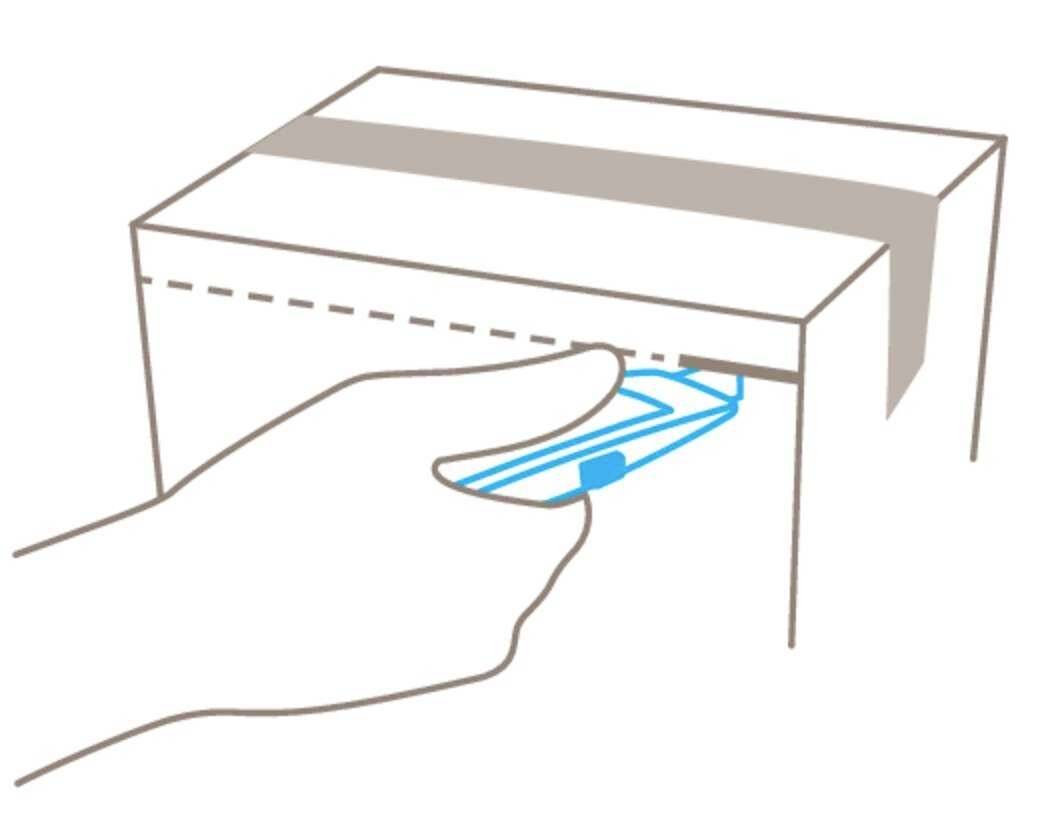 Une main retire un distributeur de serviettes en papier bleu d'une boîte rectangulaire. La boîte est scellée avec du ruban adhésif.