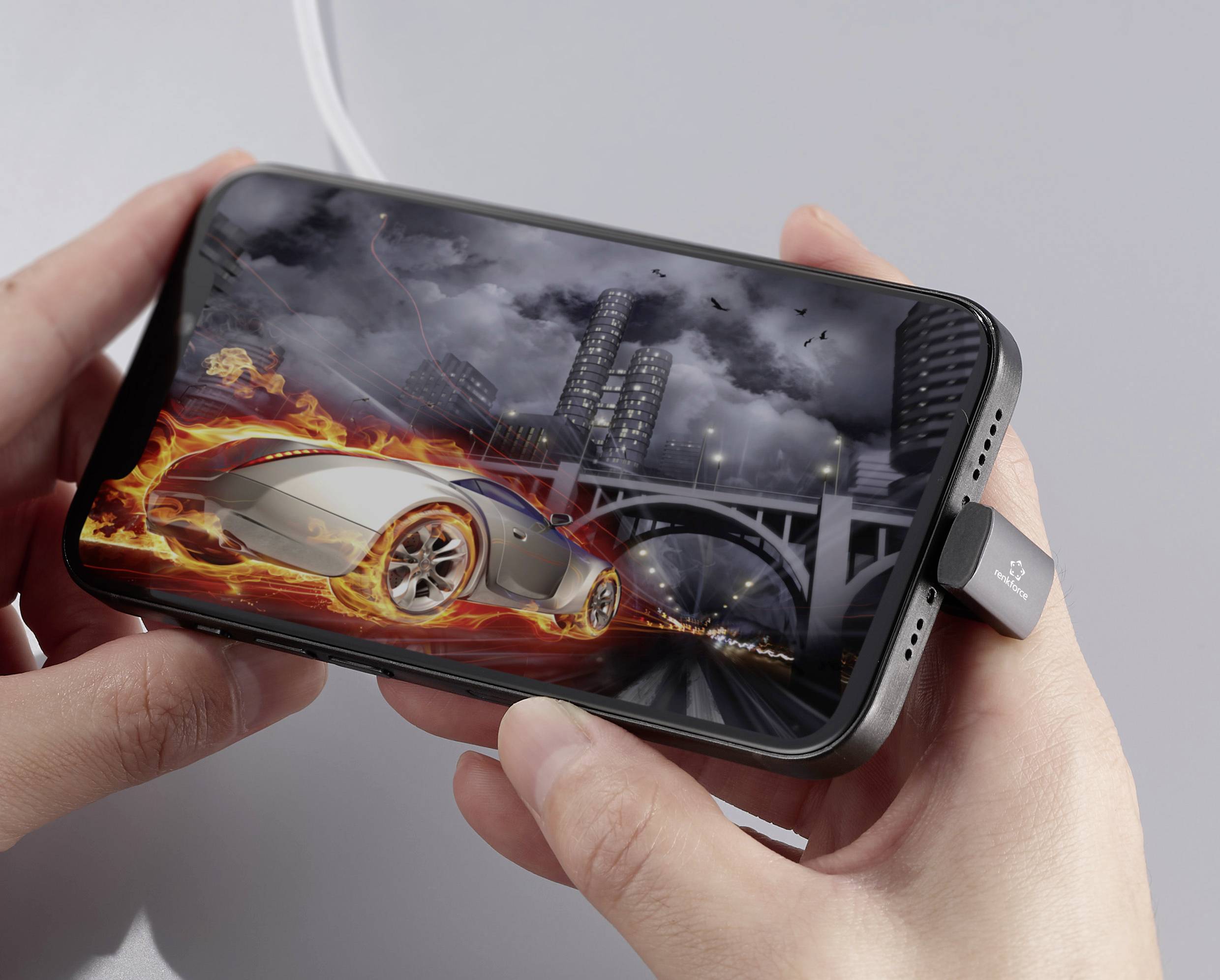 Une personne tient un smartphone affichant un jeu de course dans lequel une voiture futuriste traverse une ville illuminée.