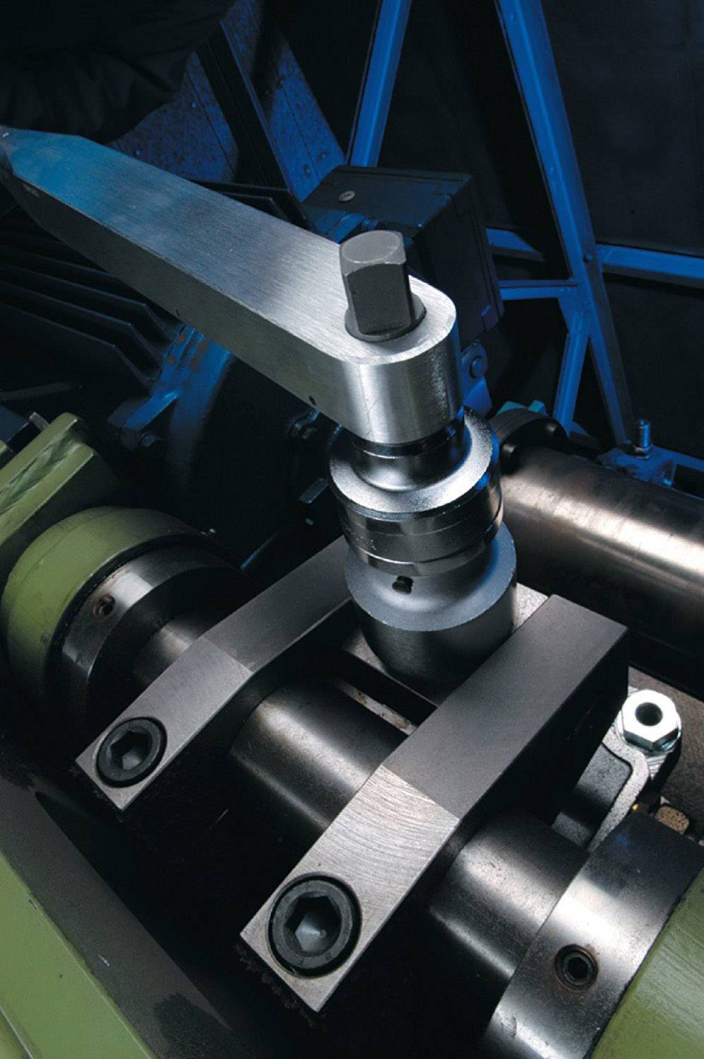 Une machine métallique équipée d'un levier qui serre une vis sur un cylindre. Elle est utilisée dans un environnement industriel.