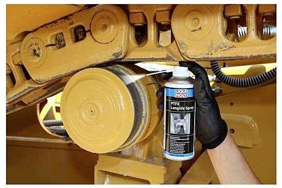 Une personne portant un gant noir vaporise « Liqui Moly PTFE Longlife Spray » sur une pièce métallique d'une machinerie, ce qui suggère un travail de maintenance.