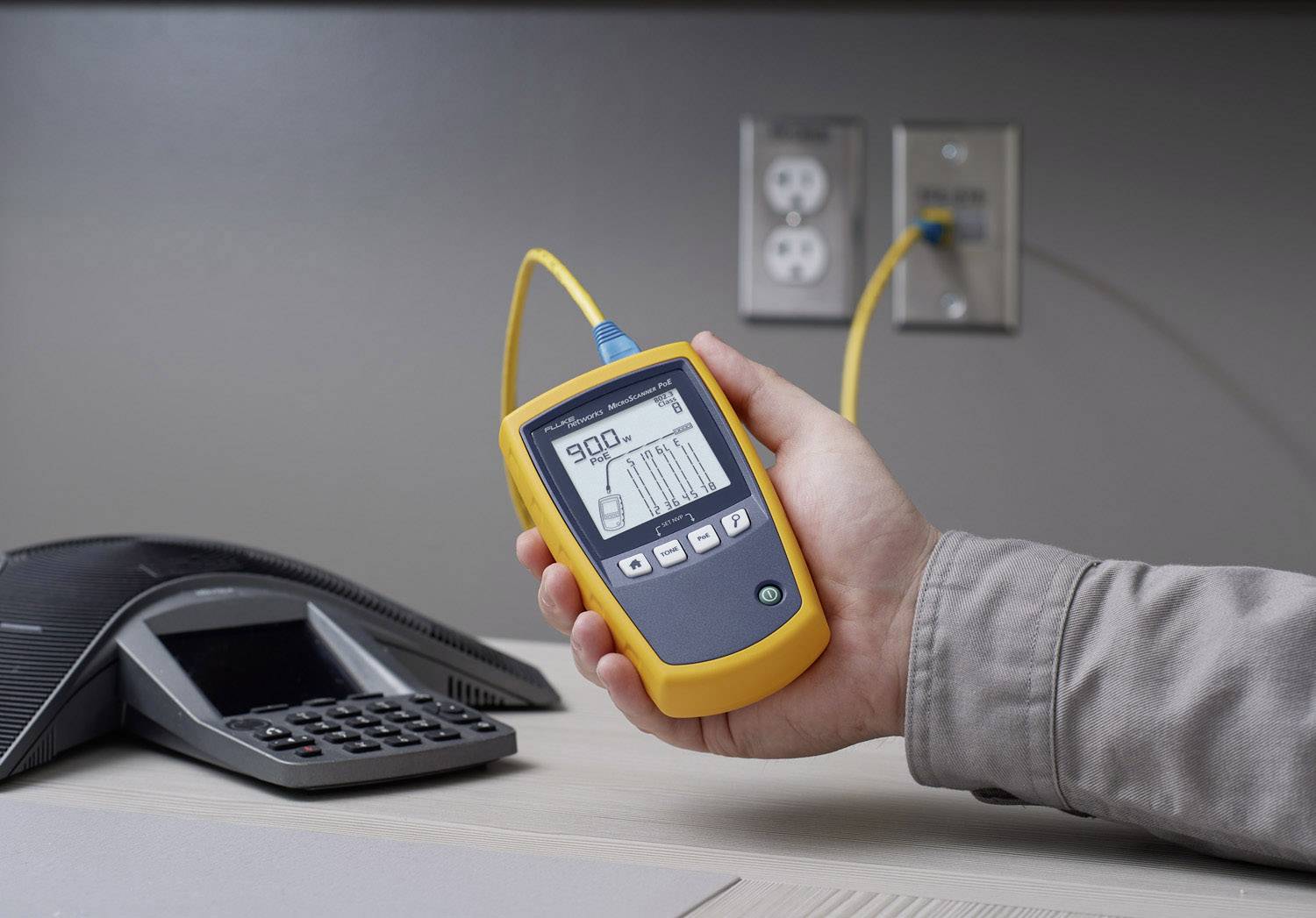 Une personne tient un appareil de test de câbles branché à une prise électrique. L'affichage indique une mesure de 900 unités.