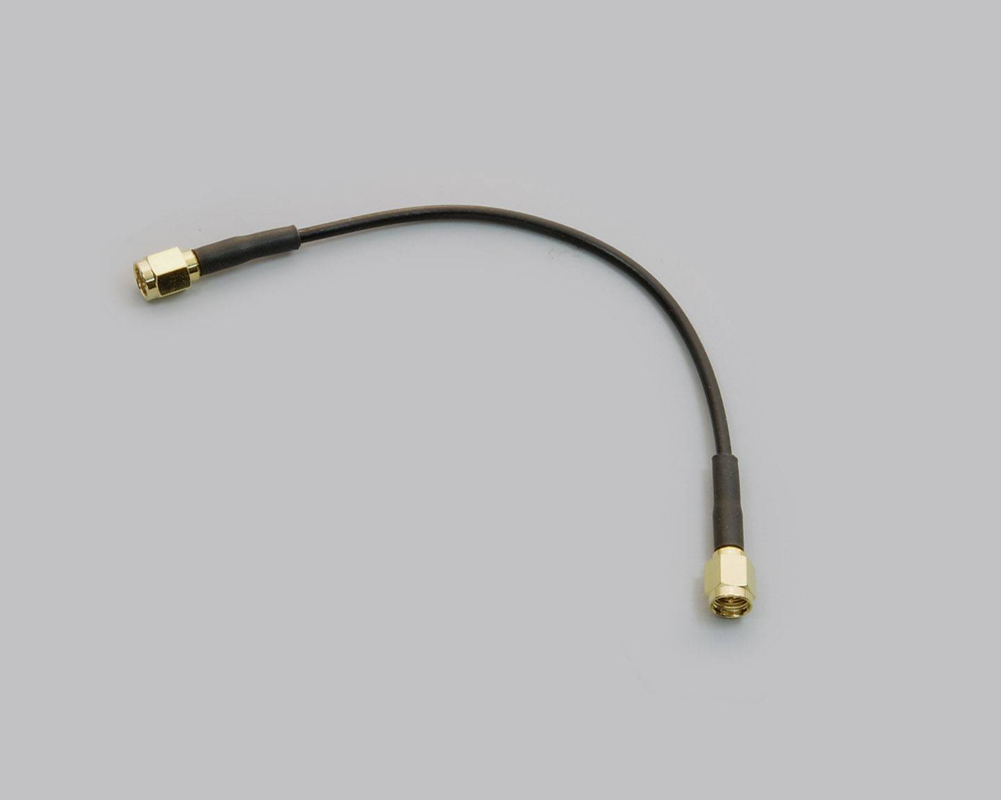 Un court câble coaxial noir avec des connecteurs dorés à chaque extrémité est posé sur un fond gris.
