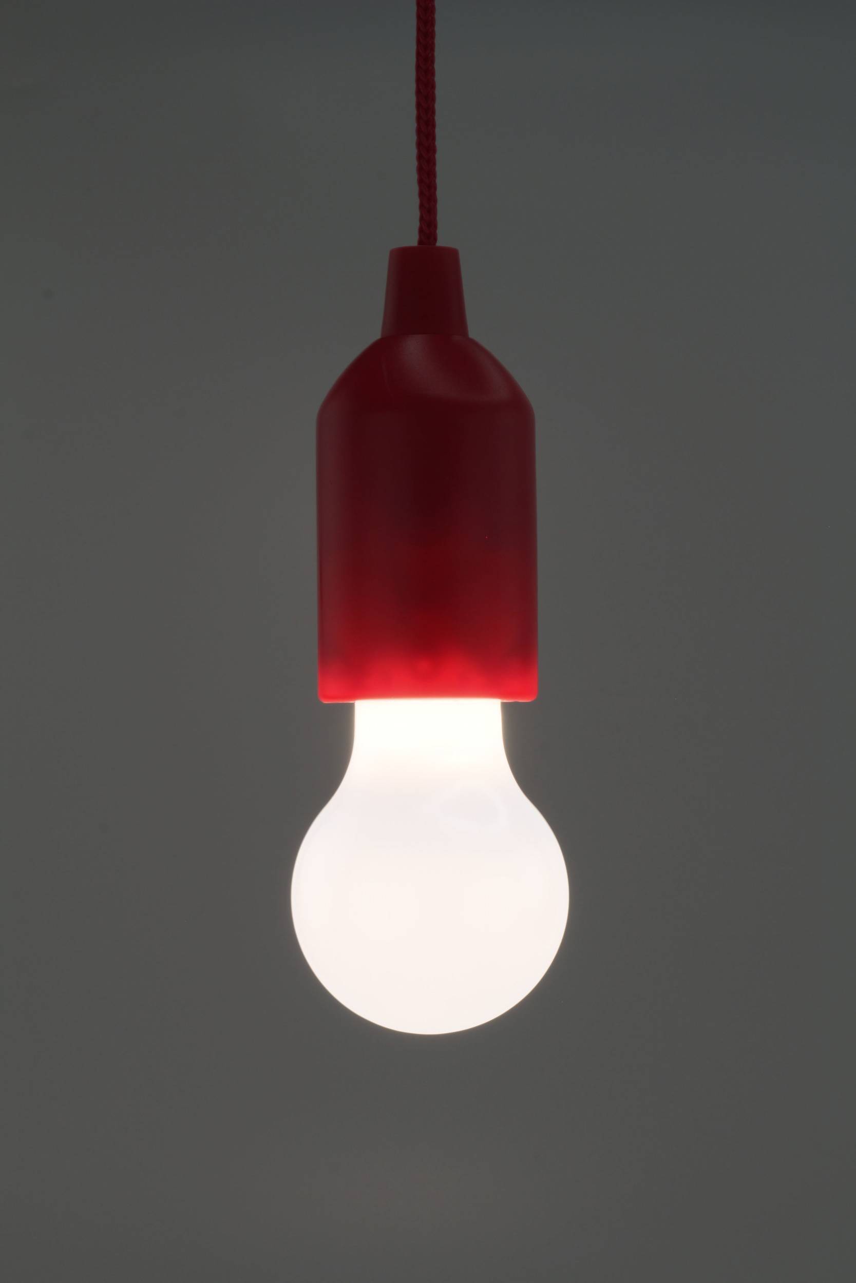 Une ampoule lumineuse avec un socle rouge pend du plafond. L'arrière-plan est sombre, l'accent étant mis sur l'ampoule comme source de lumière.