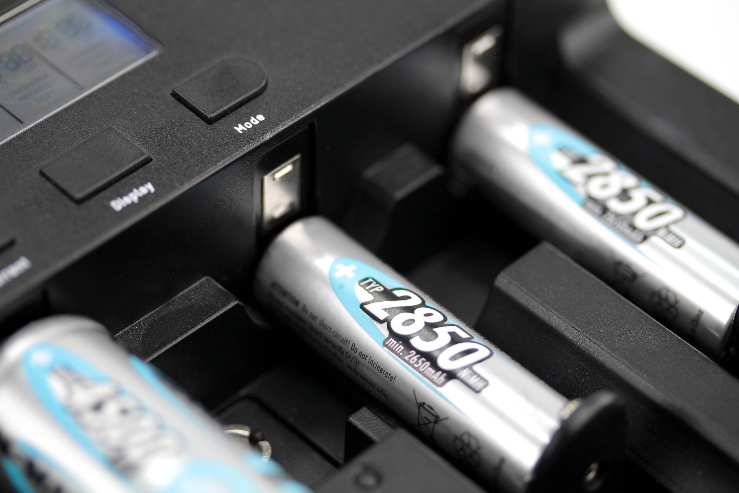 Un chargeur charge plusieurs piles AA. Deux piles sont visibles, dont une est à insérer près du chargeur.