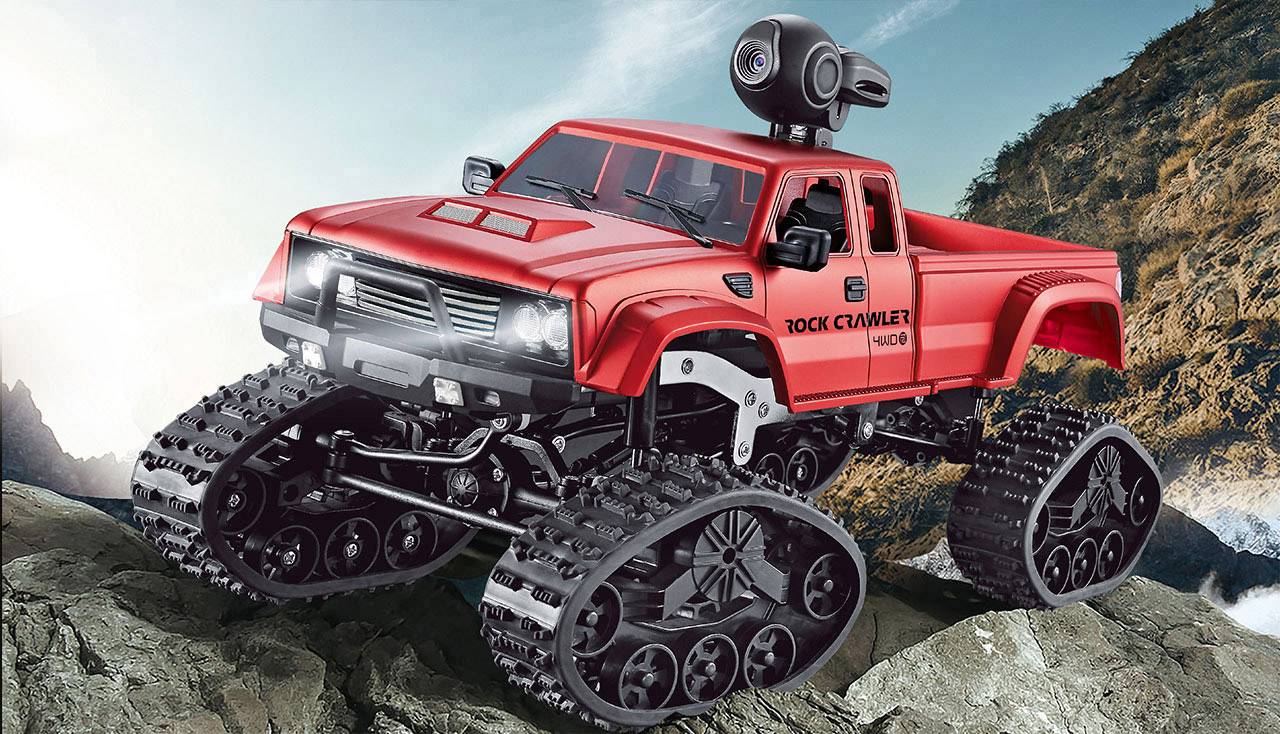 Un rock-crawler rouge télécommandé, équipé d'une chenille, traverse un terrain rocailleux devant un panorama montagneux, doté d'une caméra.