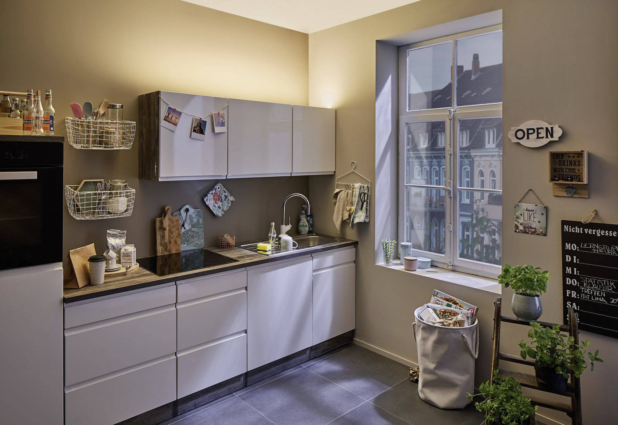 Cuisine moderne avec des armoires blanches, un évier et une grande fenêtre. Éclairage lumineux et décorations variées.