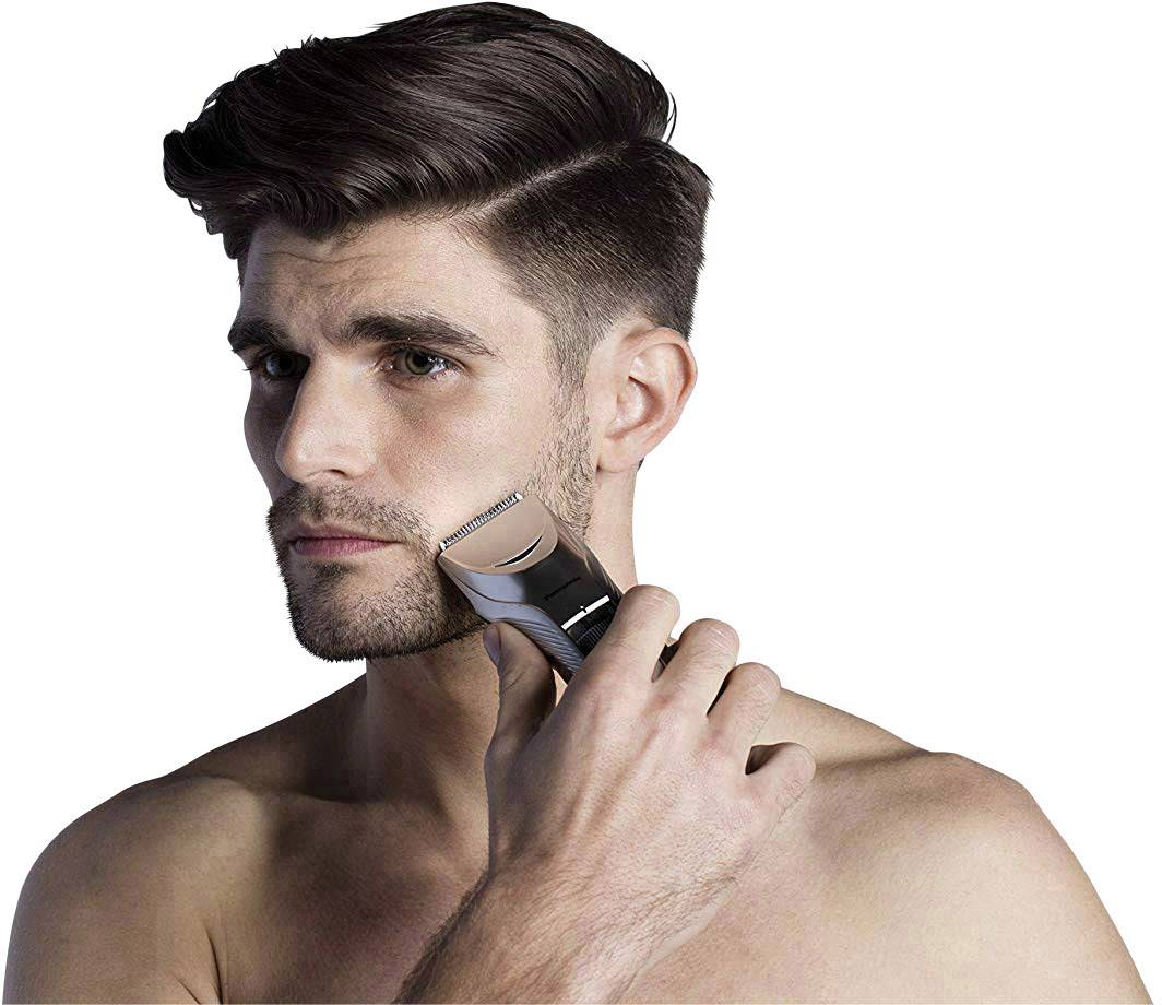 Un homme se rase le visage avec un rasoir électrique. Il a les cheveux courts et foncés, et l'arrière-plan est blanc.