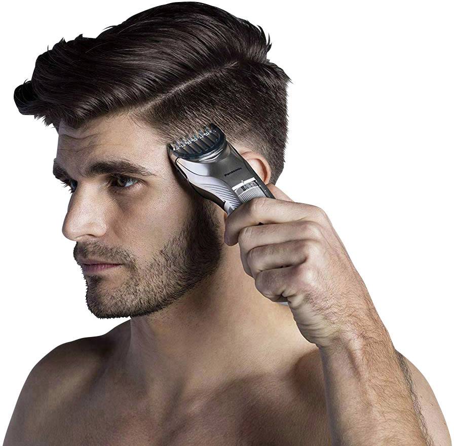 Homme à barbe coiffant ses cheveux avec une tondeuse électrique. Côtés courts, cheveux plus longs sur le dessus. Concentration sur le processus de coupe de cheveux.