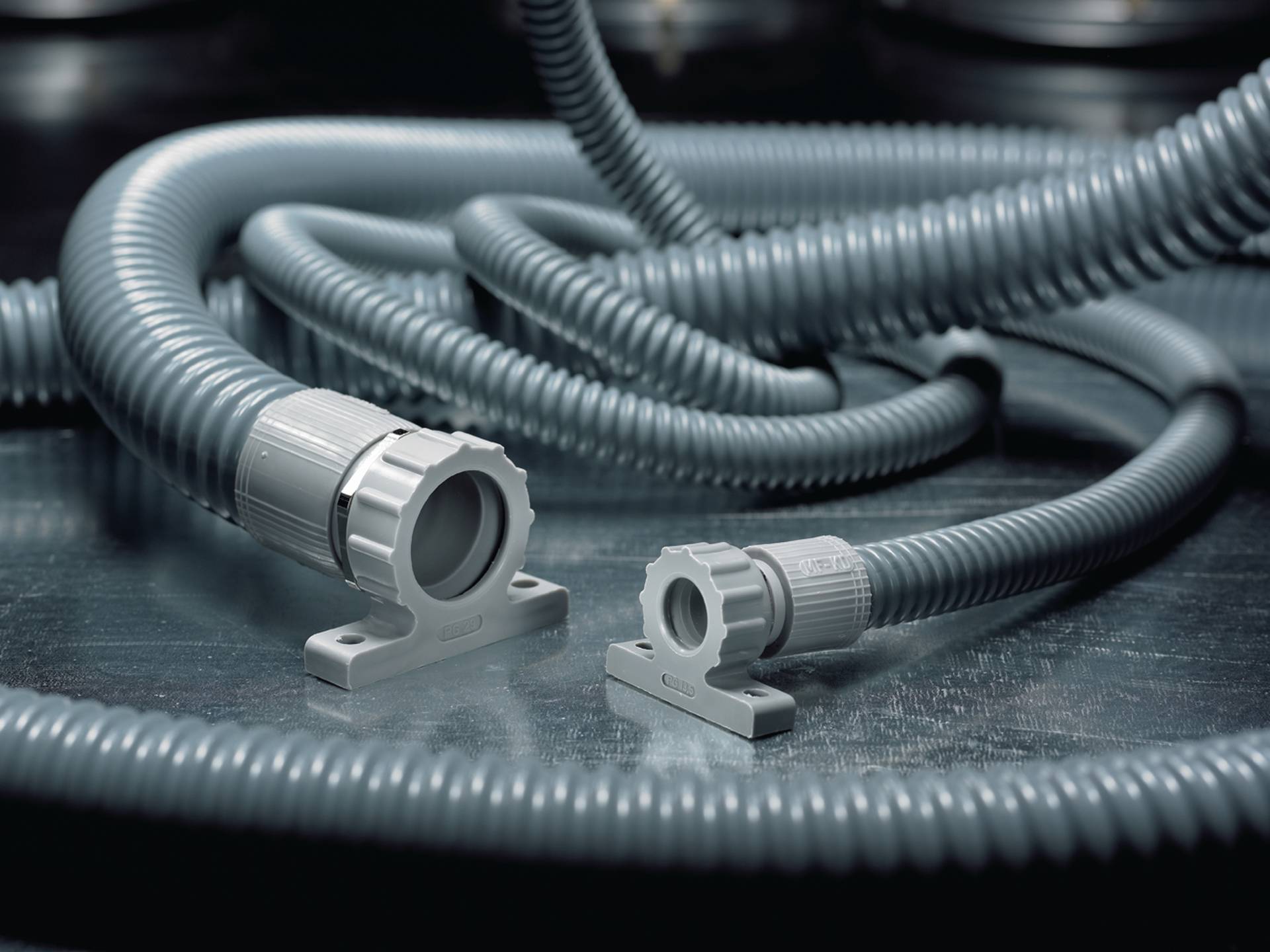 Deux tuyaux flexibles en plastique gris sur une surface métallique. L'un est plus long, l'autre plus court. Tous deux sont munis de connecteurs.