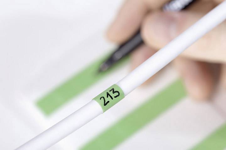 Une main tient un stylo au-dessus d'un document portant des surlignages verts. Au premier plan, on peut voir un câble portant le numéro '213'.