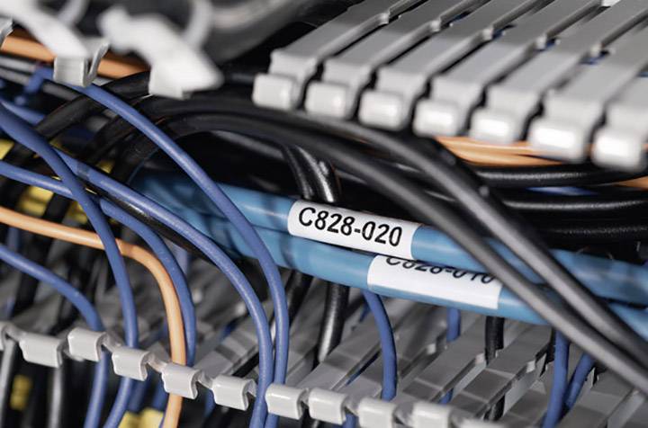 Plusieurs câbles colorés dans un rack serveur, étroitement regroupés, avec une étiquette 'C828-Q20'. Infrastructure technique dans un centre de données.