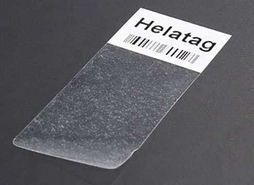 Un autocollant rectangulaire et transparent portant l'inscription 'Helatag' et un code-barres sur une surface sombre.