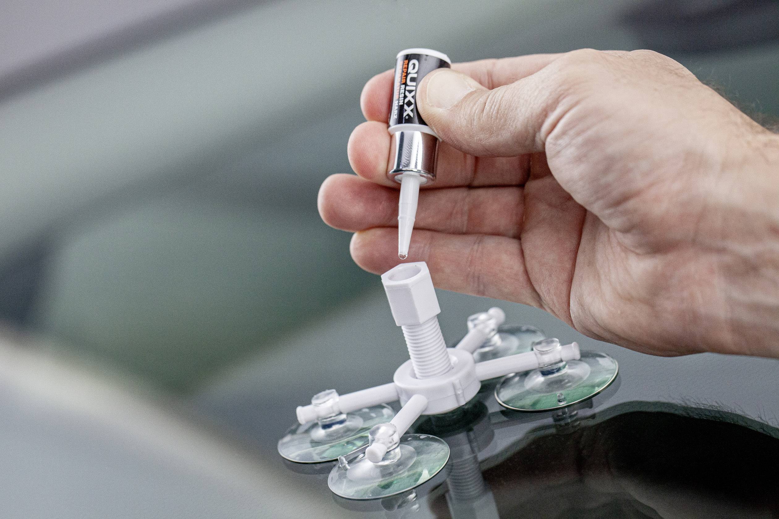 Une main tient un tube de colle au-dessus d'un outil de réparation à ventouses pour vitrage automobile, pendant que la colle est versée à l'intérieur.