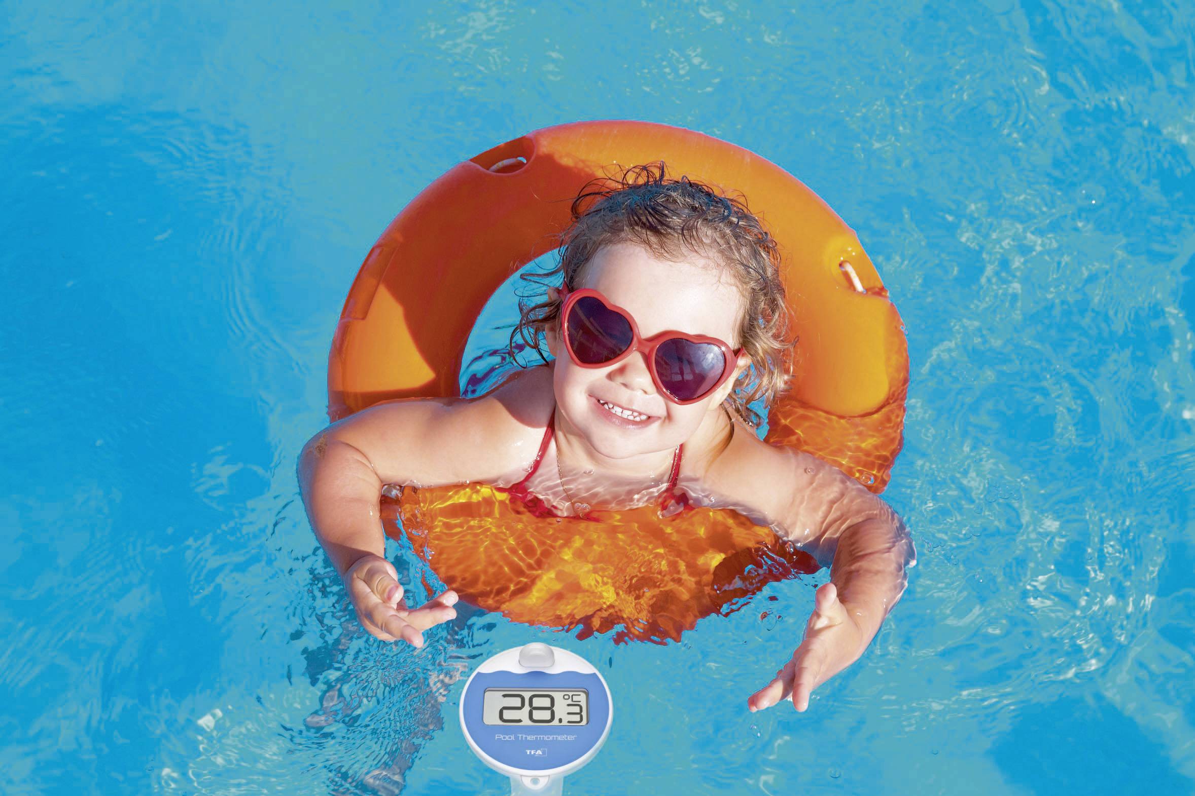 Petit enfant portant des lunettes de soleil rouges, nageant joyeusement dans une bouée orange au milieu de l'eau bleue de la piscine. L'affichage de température indique 28,3°C.