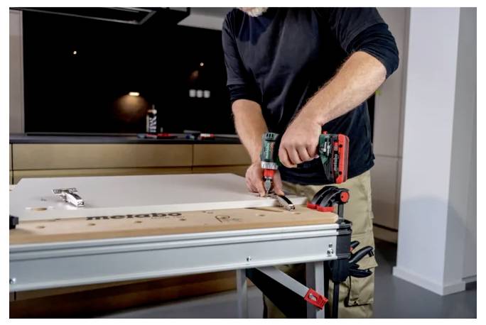 Homme utilisant une perceuse sans fil pour assembler un grand établi en métal ou un placard dans un espace de travail intérieur moderne.
