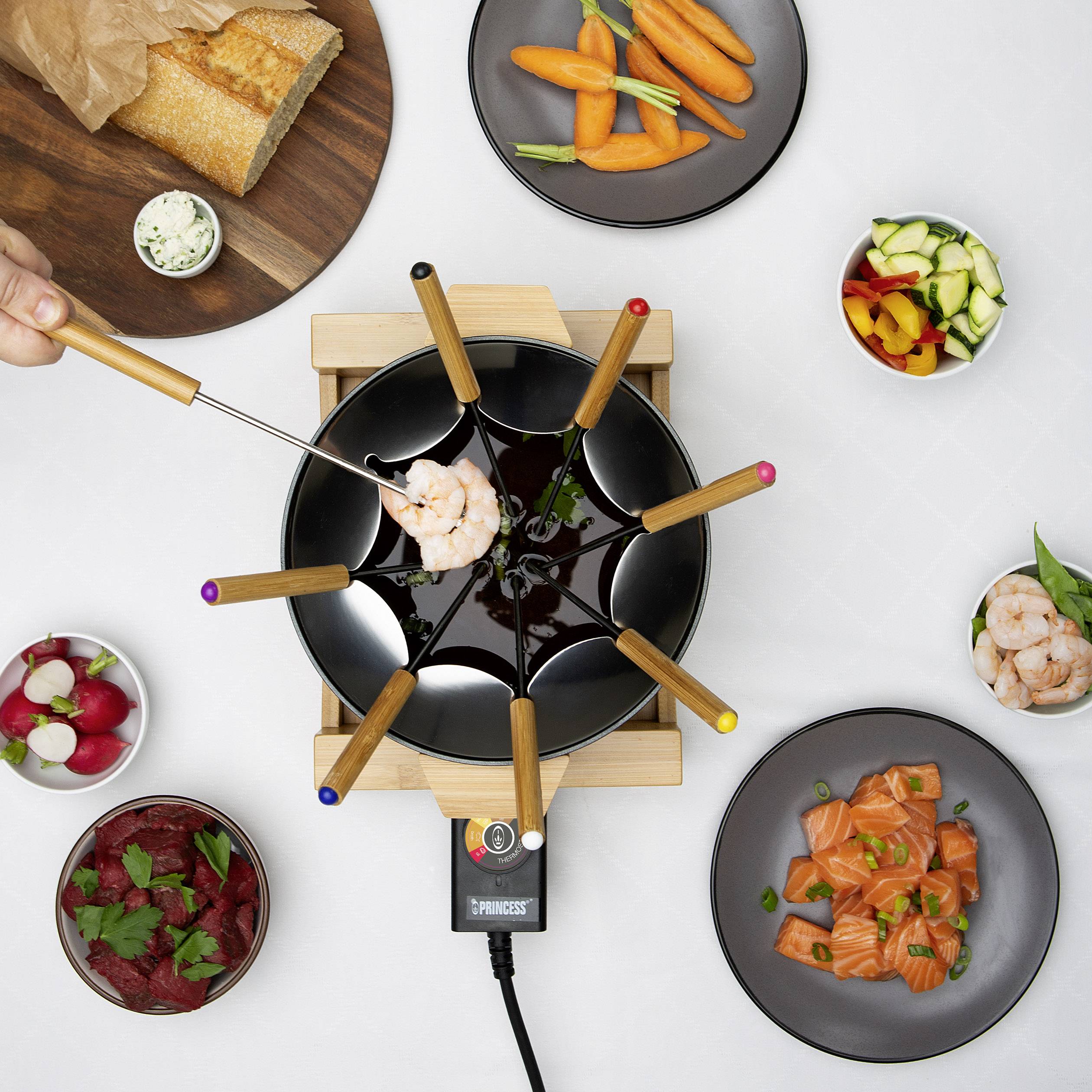 Un set à fondue avec différents ingrédients comme des crevettes, des légumes et du pain sur une table.