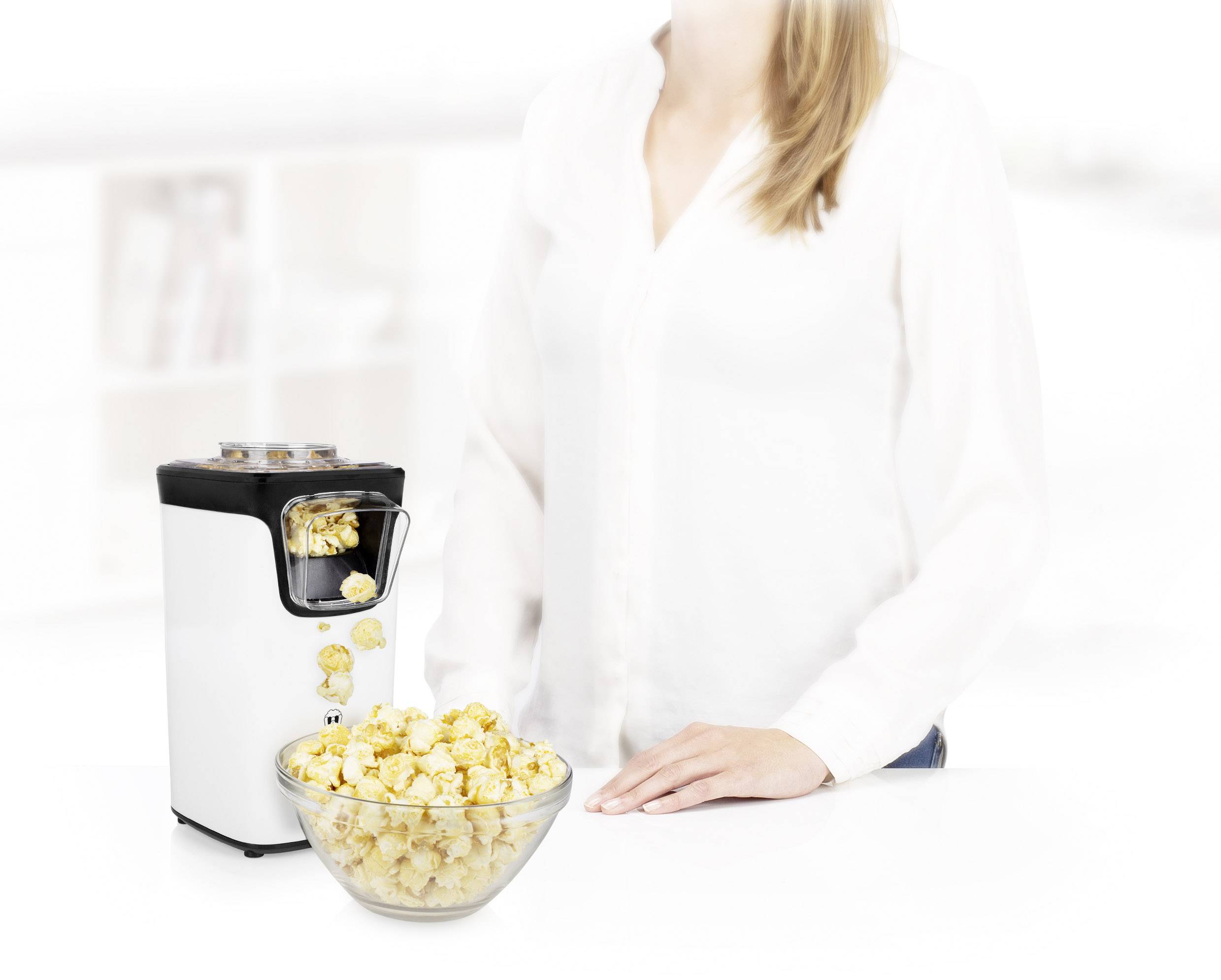 Une personne se tient à côté d'une machine à pop-corn posée sur une table. Devant la machine se trouve un bol rempli de pop-corn fraîchement préparé.