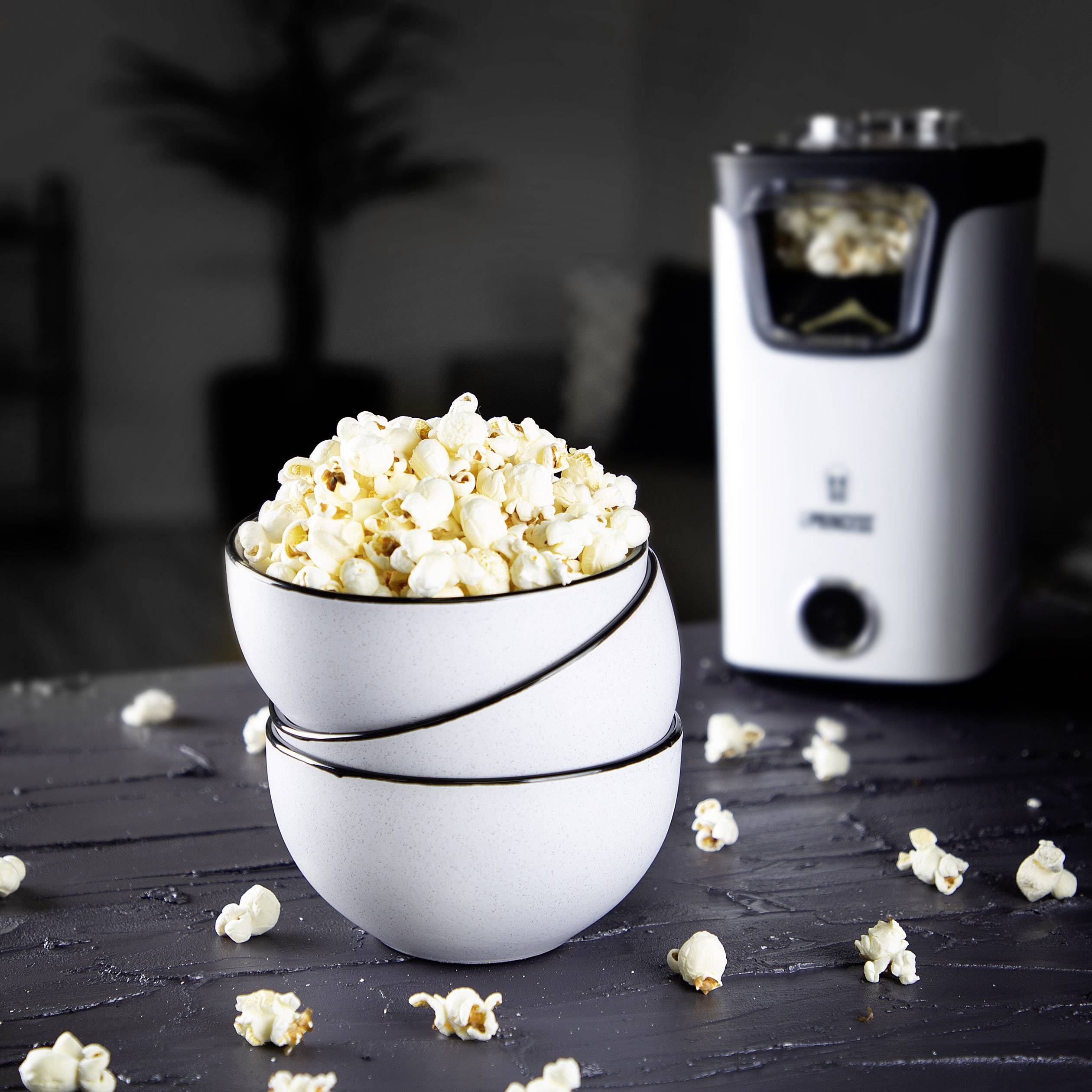 Un bol de pop-corn frais est posé sur une table, avec une machine à pop-corn en arrière-plan.