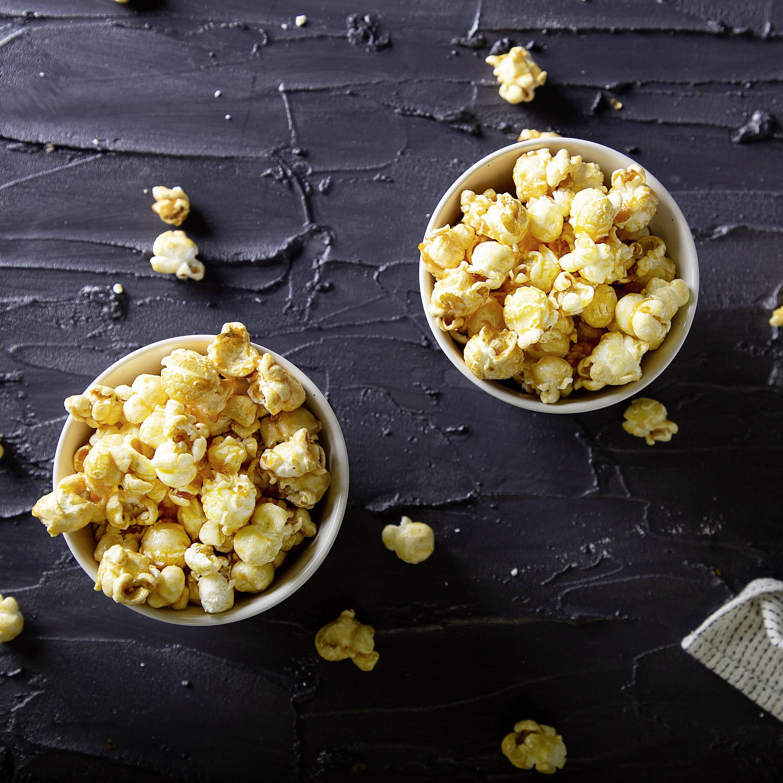 Deux bols de pop-corn fraîchement éclaté sur un fond sombre, avec quelques grains de pop-corn dispersés tout autour.