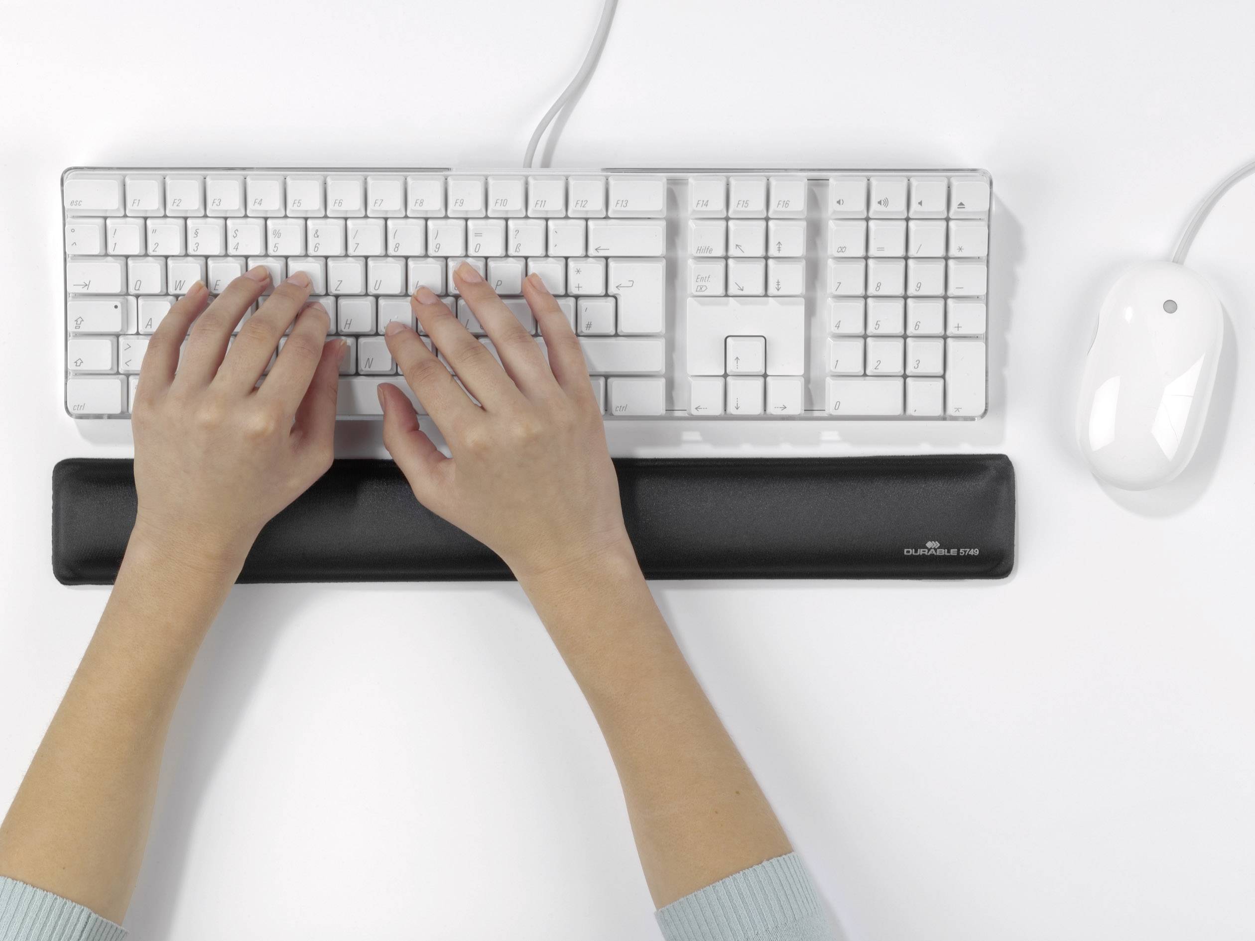 Une personne tape sur un clavier blanc avec une souris à côté. Un repose-poignets noir soutient les mains.