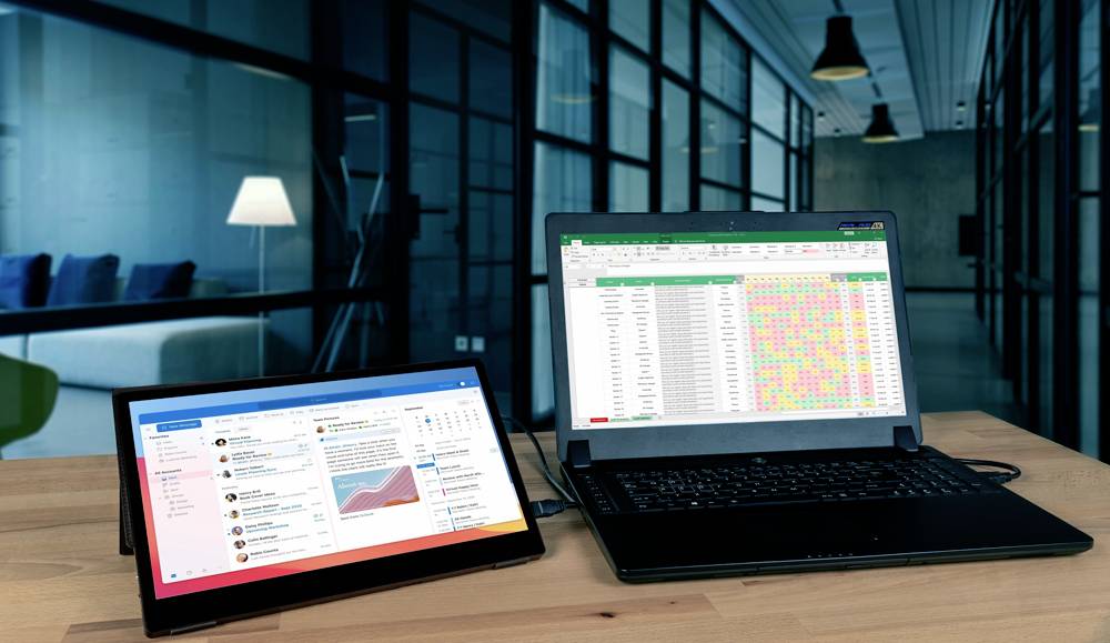 Deux ordinateurs portables sur une table dans un bureau moderne. L'écran de gauche affiche une application de messagerie, celui de droite un tableur coloré.