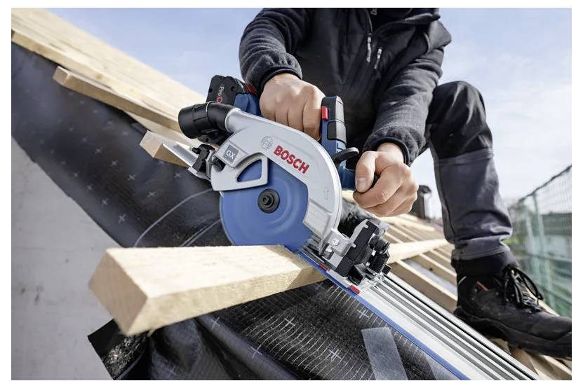 Une personne utilise une scie circulaire Bosch pour couper des planches en bois sur un toit en pente, portant un équipement de protection et concentrée sur une coupe précise.