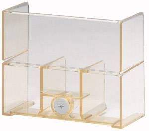 Un objet en plastique transparent et jaunâtre, comportant plusieurs compartiments et une petite horloge ronde au centre.