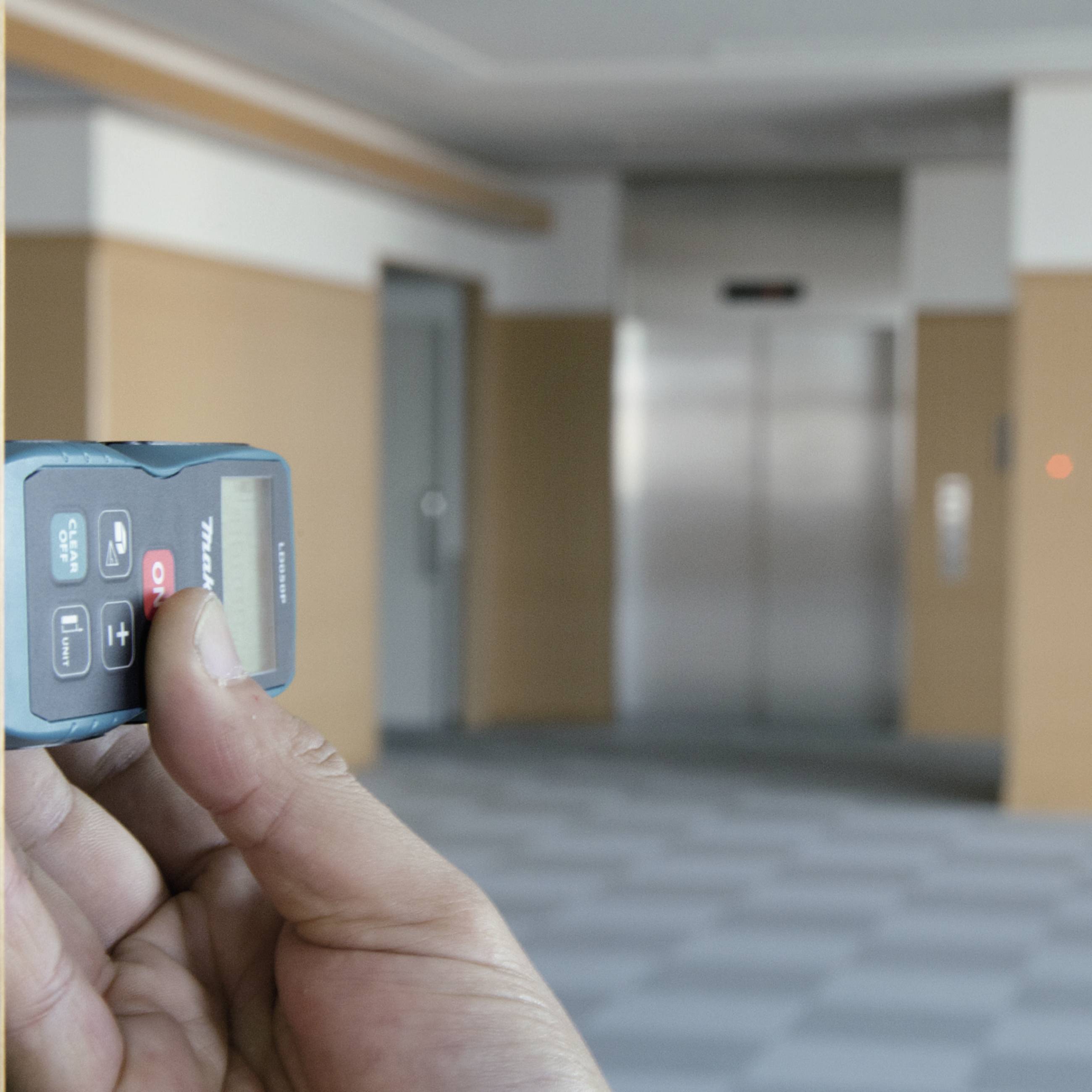 Une main tient une télécommande à l'intérieur d'un bâtiment, avec un ascenseur visible en arrière-plan.